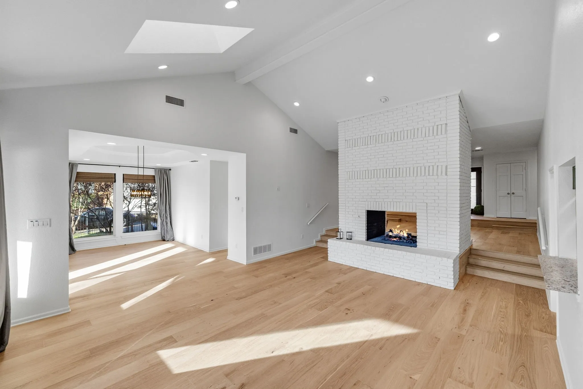 Unfurnished living room with light wood-style floors, a brick fireplace, a skylight, and recessed lighting