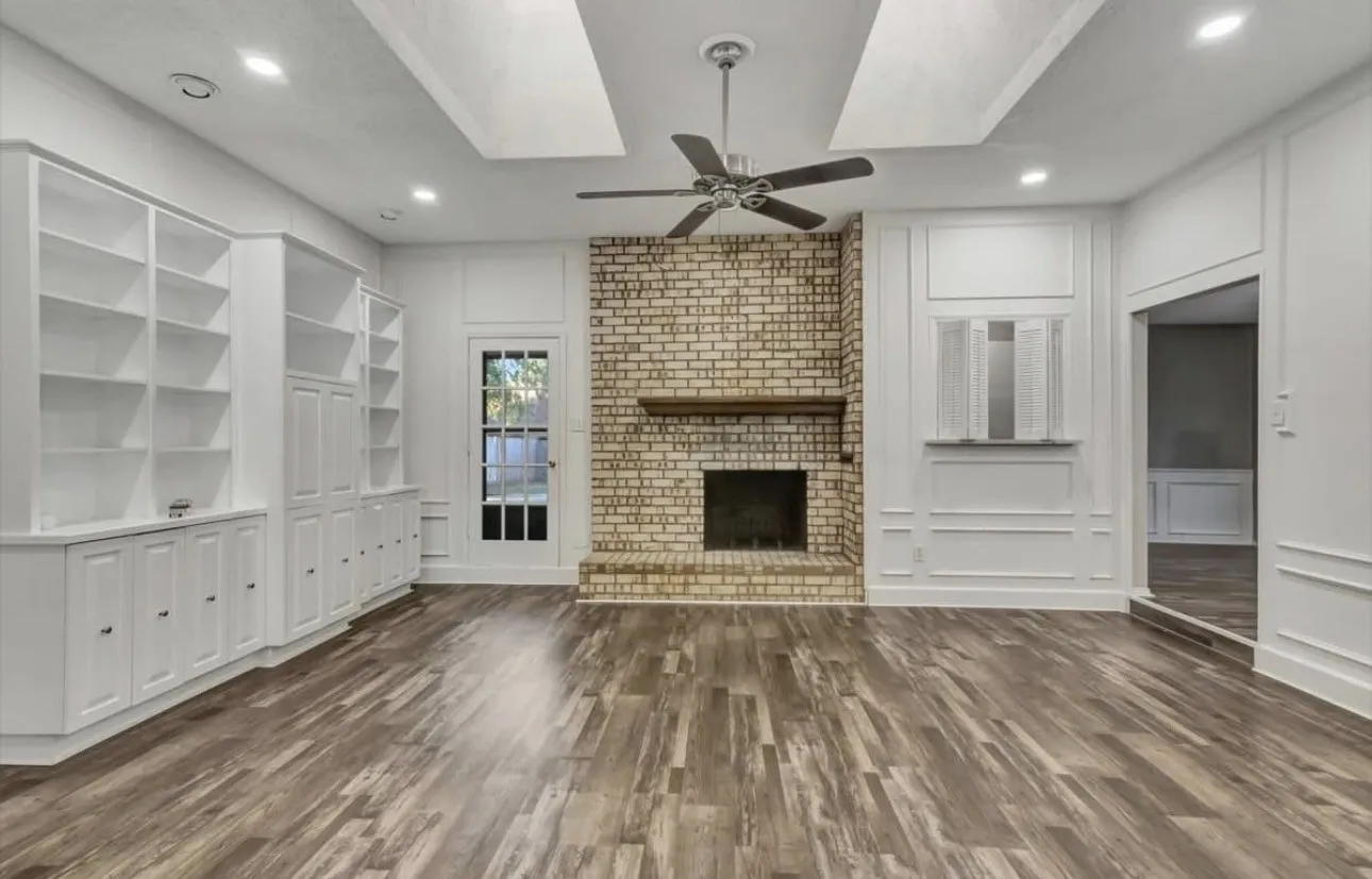 Unfurnished living room featuring a decorative wall, a ceiling fan, dark wood-type flooring, built in features, and a fireplace