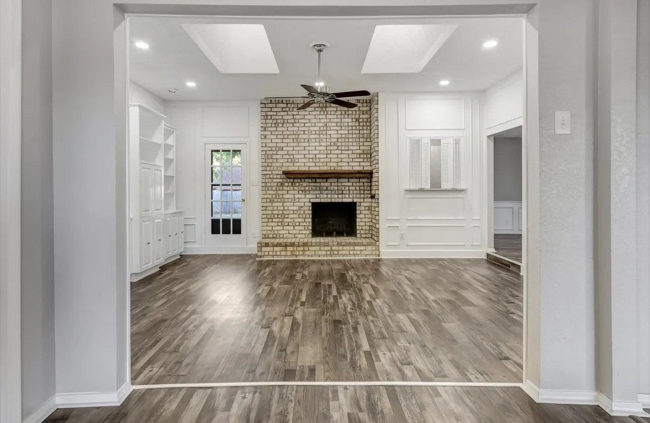 Unfurnished living room featuring a decorative wall, a fireplace, ceiling fan, dark wood-style flooring, and a skylight