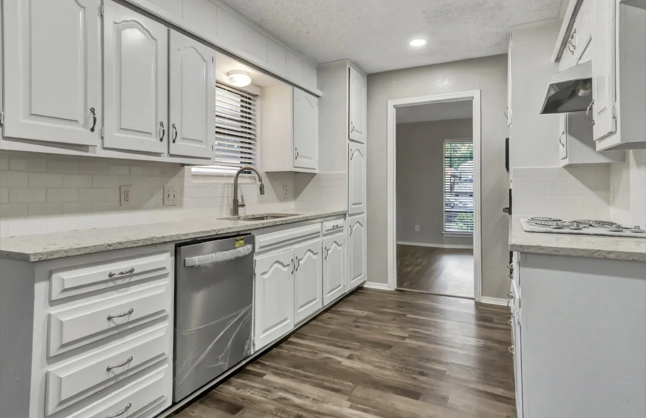 Kitchen with light stone countertops, dishwasher, decorative backsplash, white cabinets, and a textured ceiling