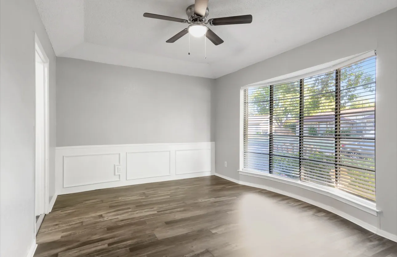 Empty room featuring ceiling fan, dark wood finished floors, a tray ceiling, and wainscoting