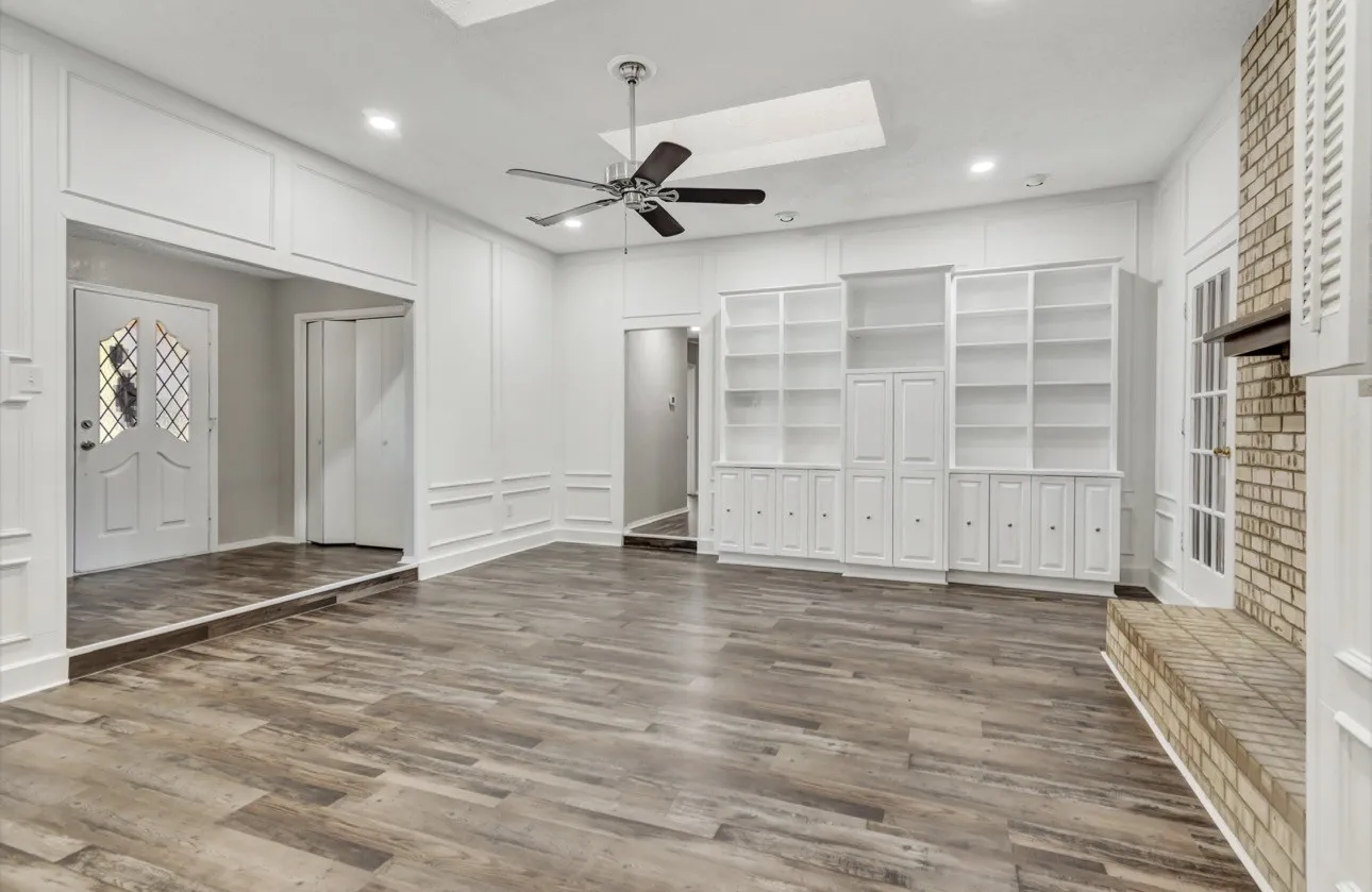 Unfurnished living room with ceiling fan, a decorative wall, dark wood finished floors, a skylight, and recessed lighting