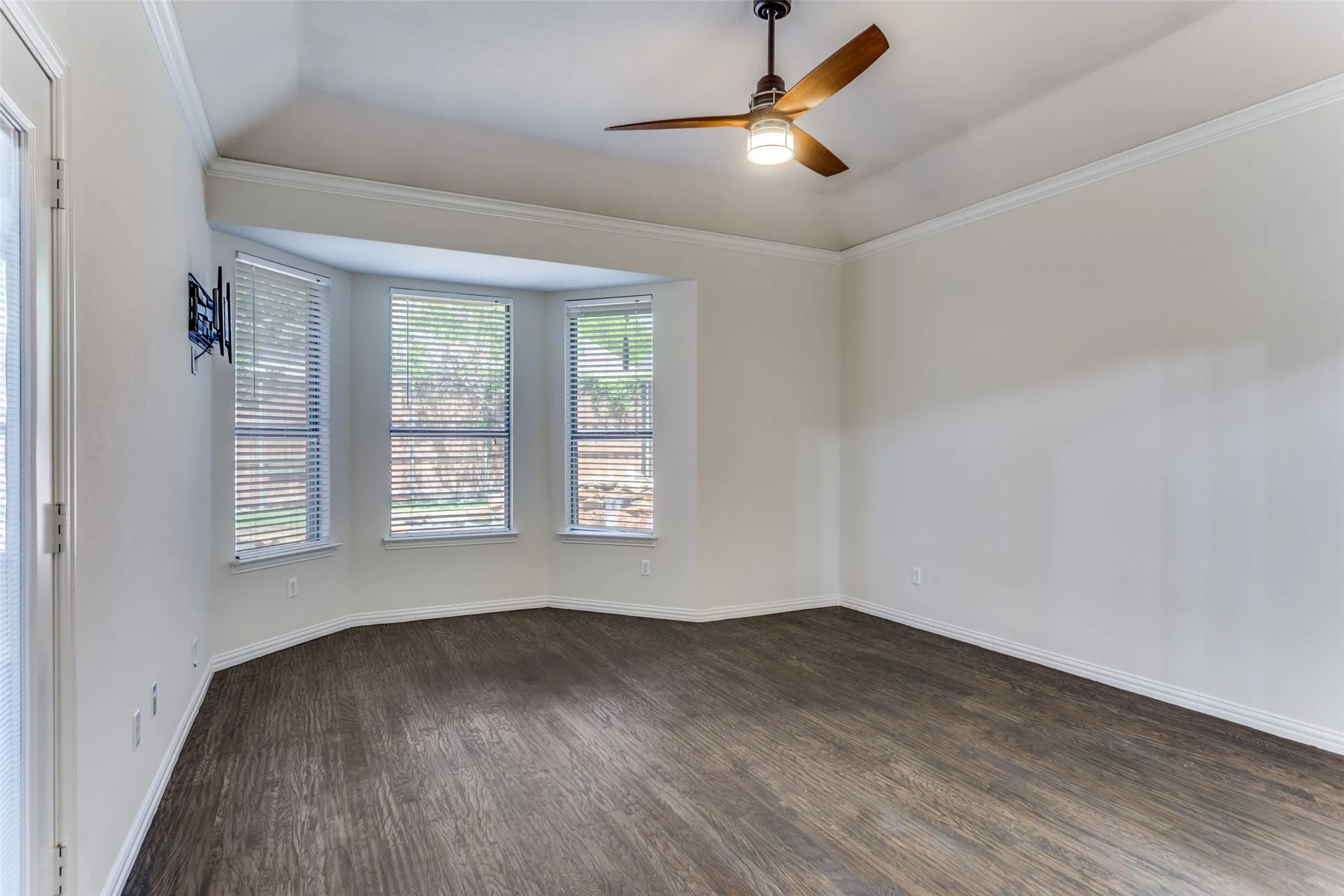 Primary bedroom featuring ornamental molding, raised ceiling, a ceiling fan, and dark wood-type flooring