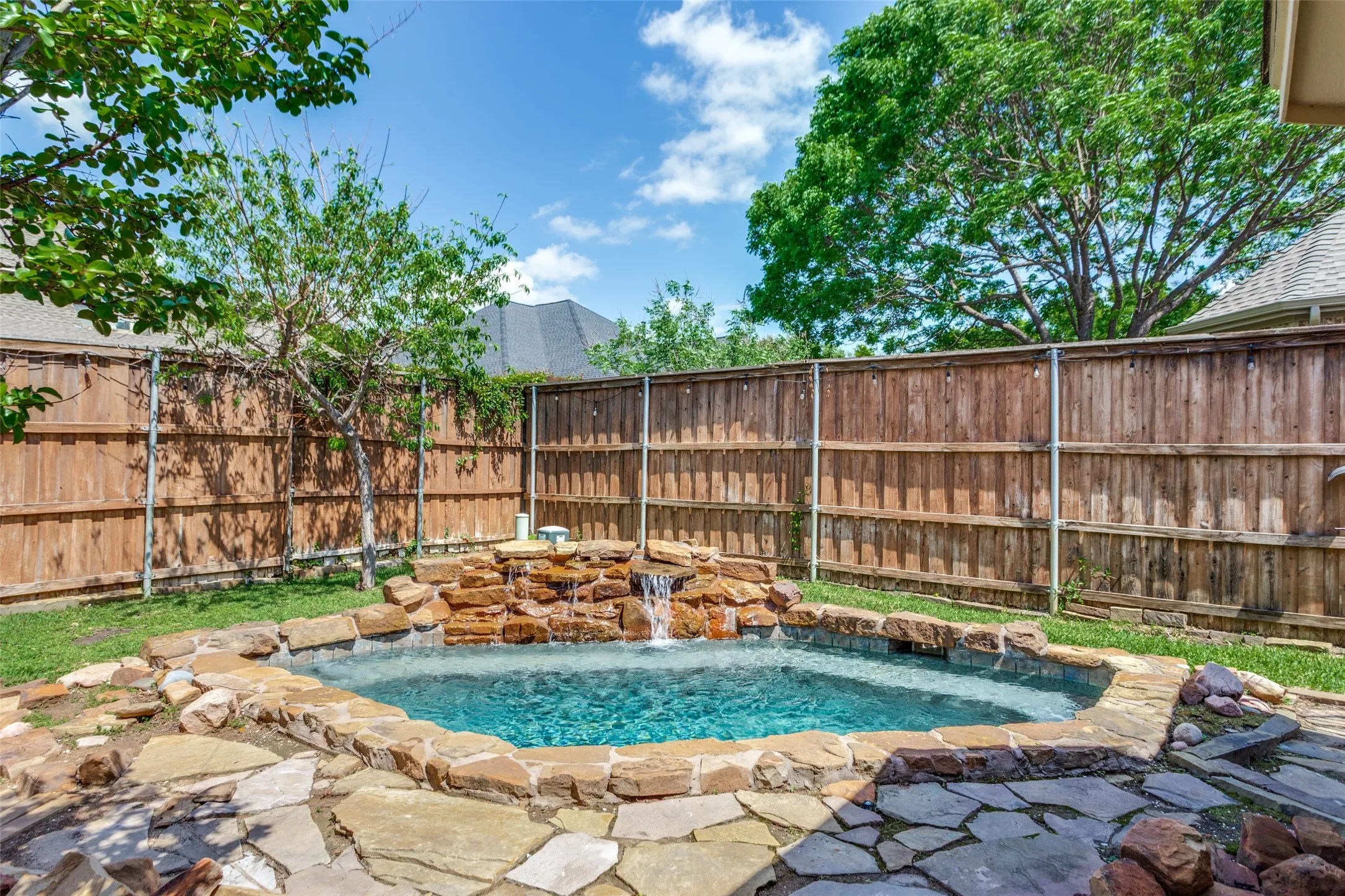 Outdoor heated spa/pool with water feature,  a fenced backyard, and a patio area.