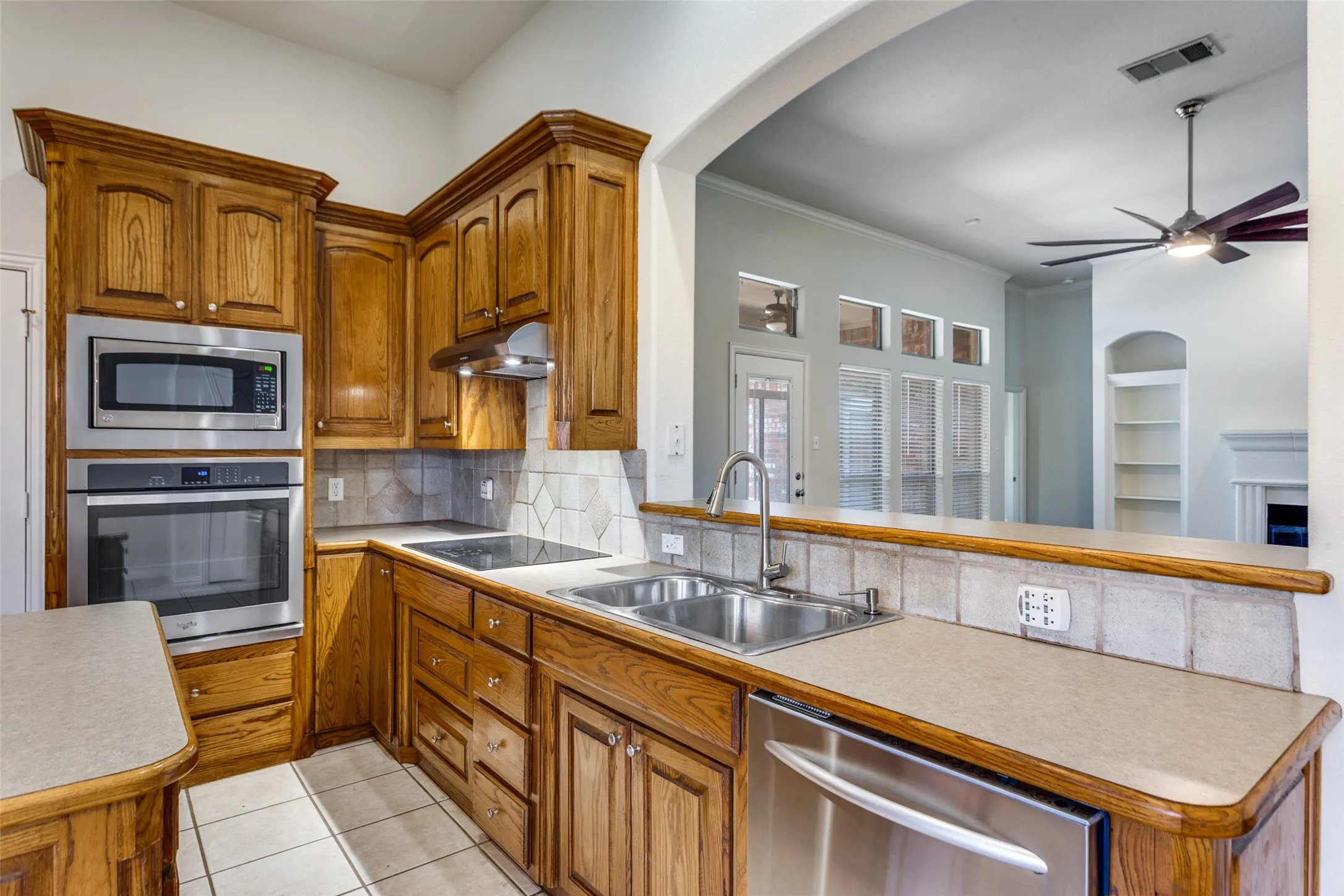 Kitchen featuring wood finish cabinets, stainless steel appliances, a ceiling fan, light countertops, and crown molding