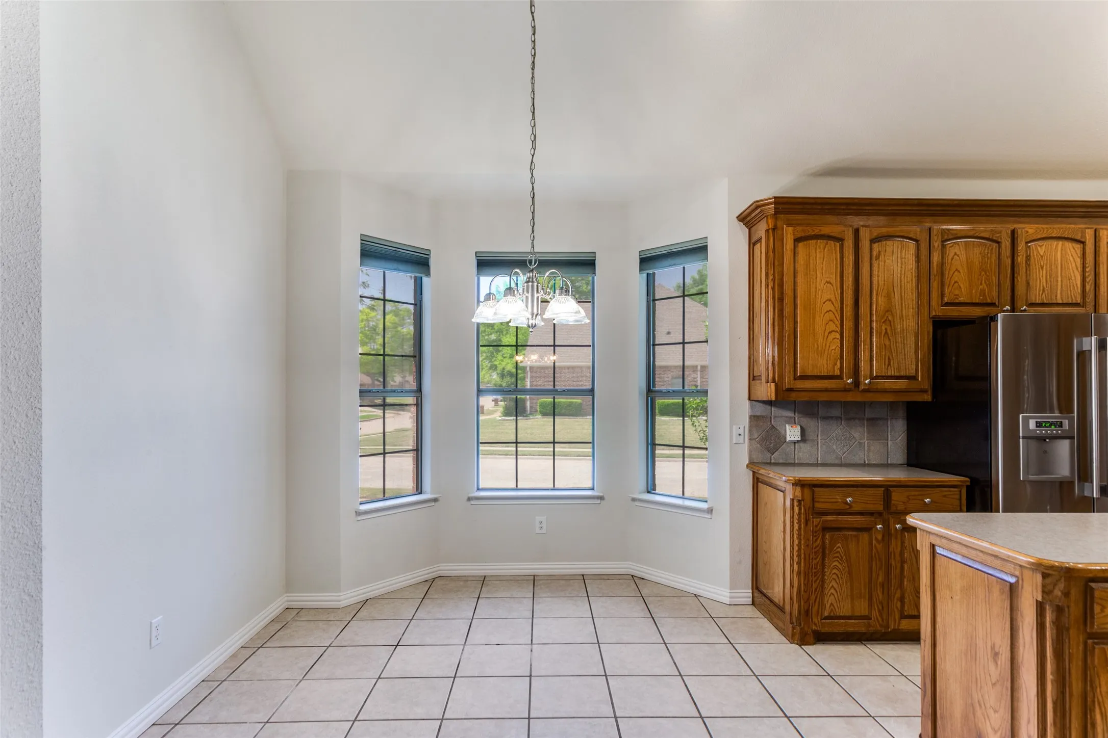 Eat in dining area,  wood finish cabinets, stainless steel refrigerator with ice dispenser, hanging lights, tasteful backsplash, and light tile patterned floors