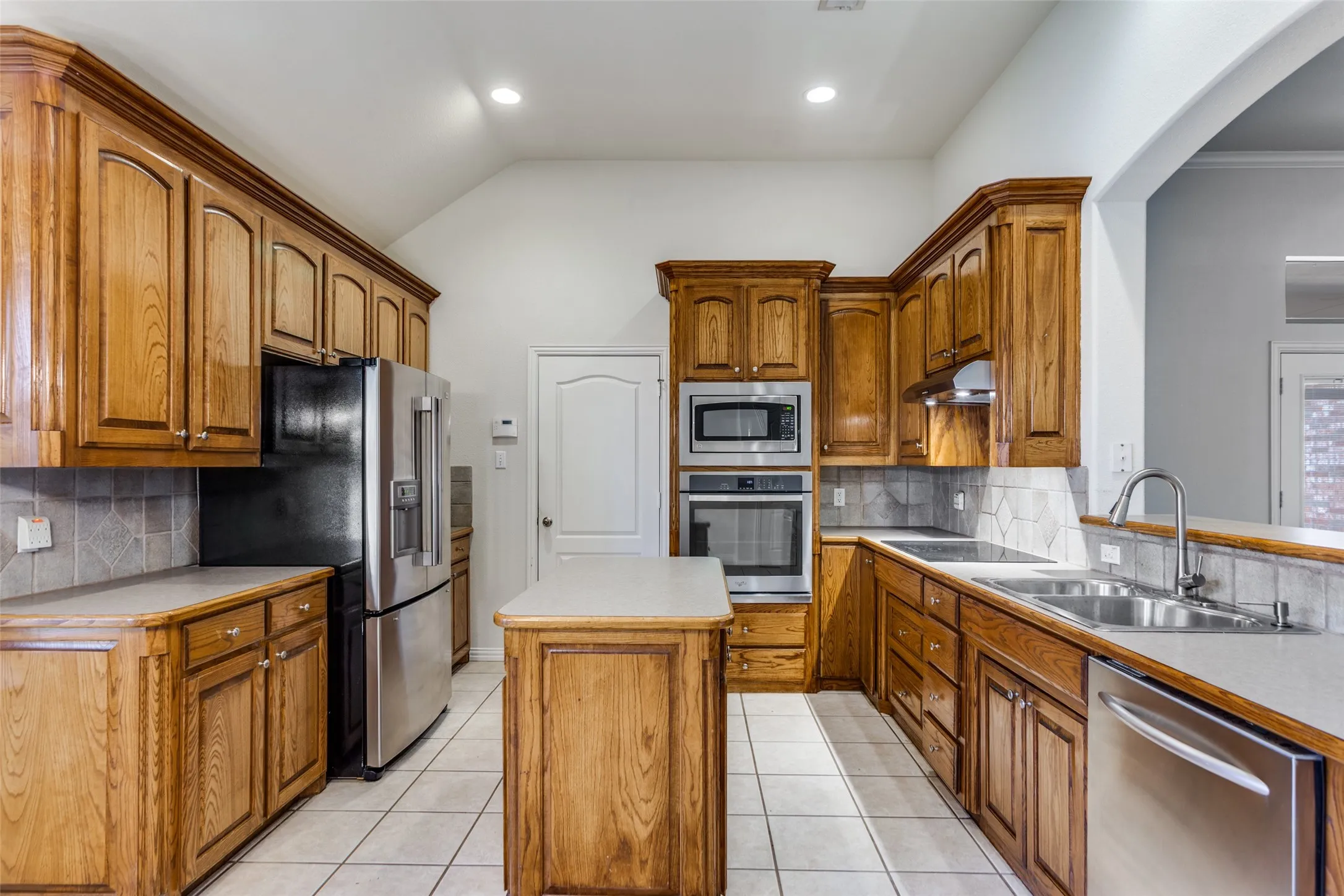 Kitchen featuring wood finish cabinetry, decorative backsplash, stainless steel appliances, recessed lighting, and vaulted ceiling