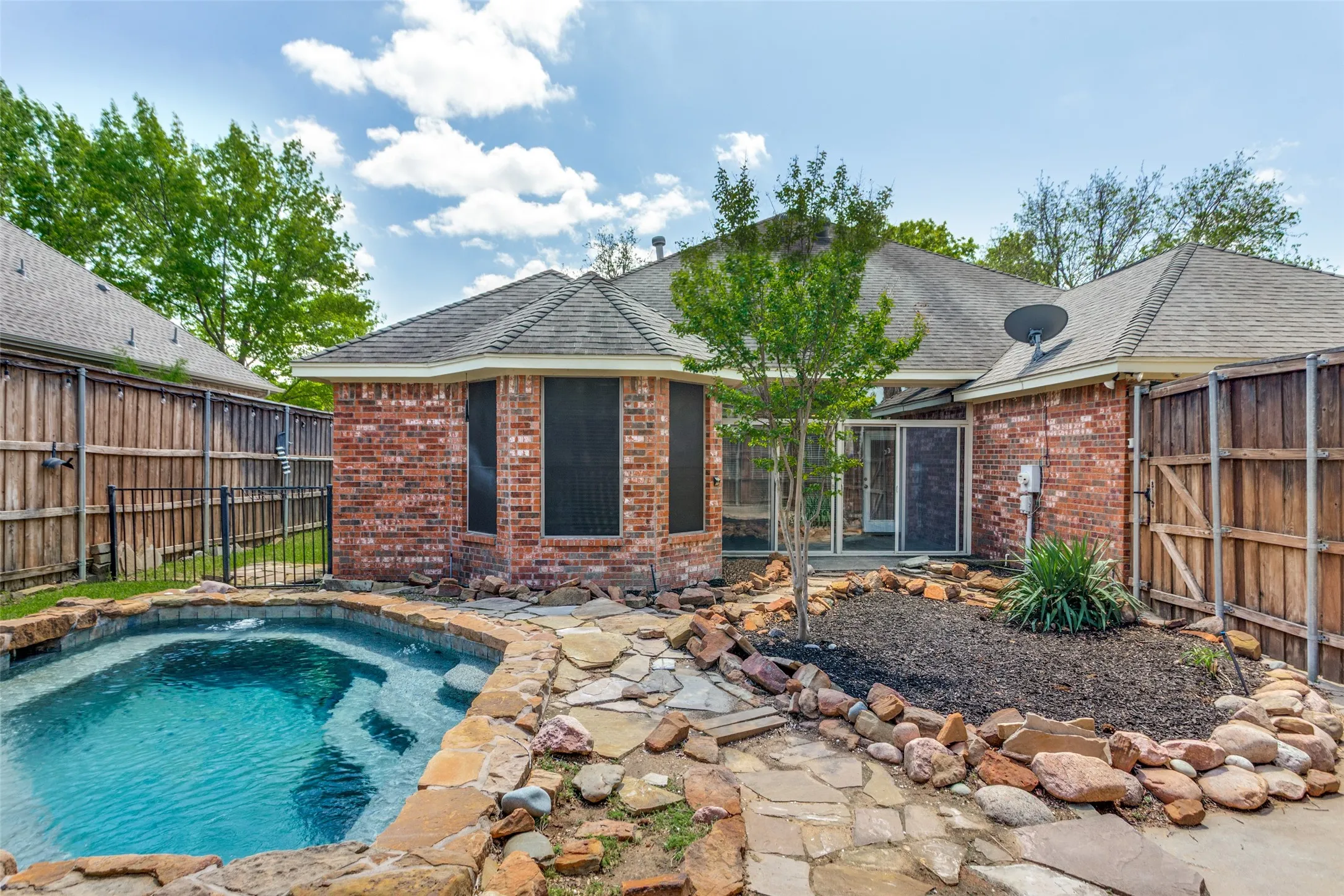 Rear view of house featuring brick siding, a fenced backyard, pool with water feature, backyard landscaping and patio area.