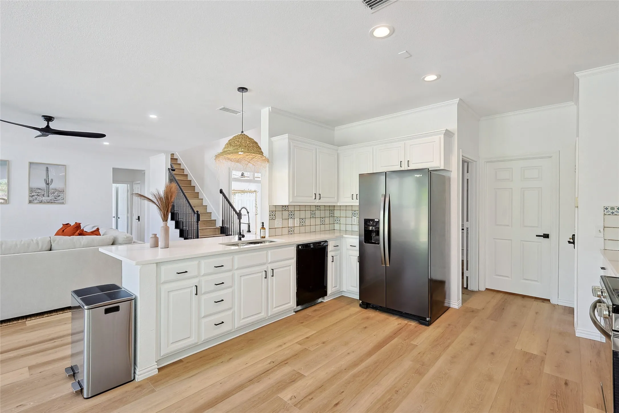 Kitchen with light hardwood / wood-style floors, stainless steel fridge, white cabinets, kitchen peninsula, and pendant lighting