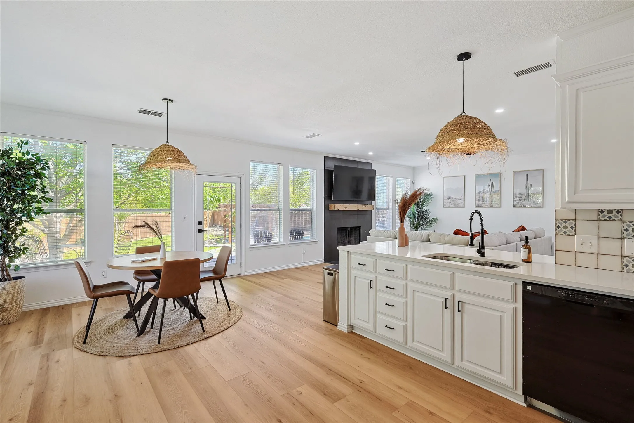 Kitchen with white cabinetry, light wood-type flooring, decorative light fixtures, sink, and black dishwasher