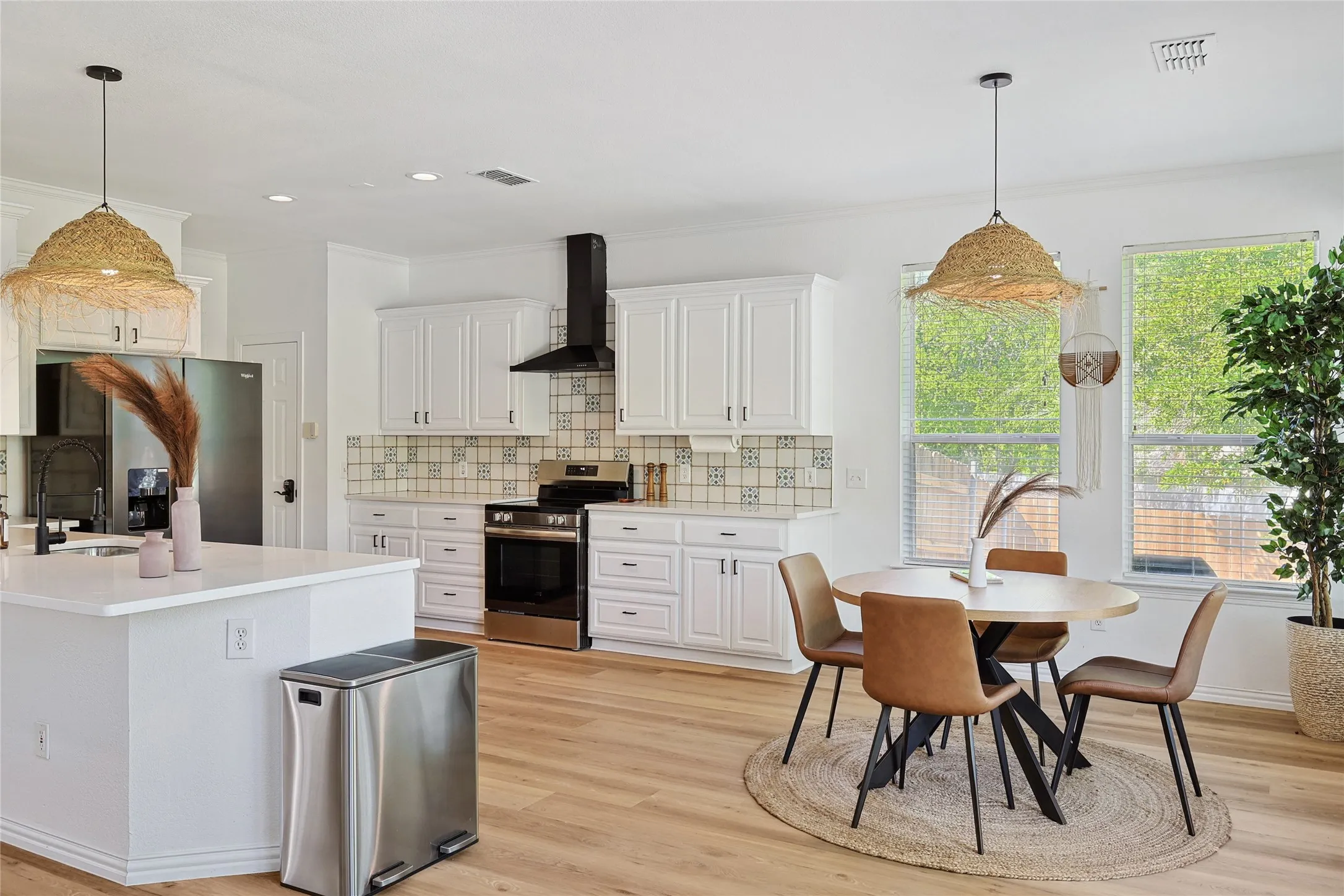 Kitchen with backsplash, appliances with stainless steel finishes, light hardwood / wood-style flooring, and wall chimney range hood