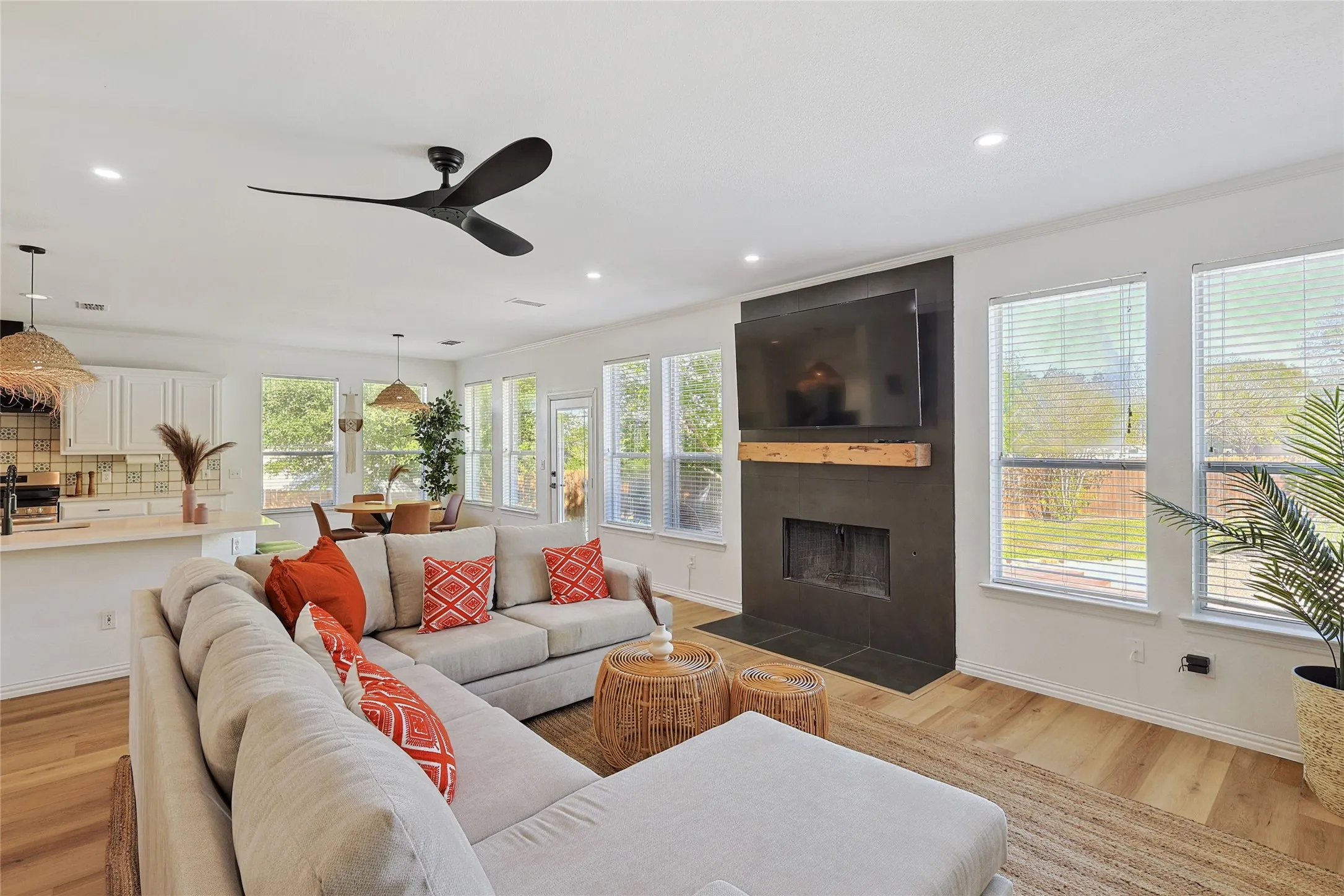 Living room with ceiling fan, a tiled fireplace, light wood-type flooring, and ornamental molding
