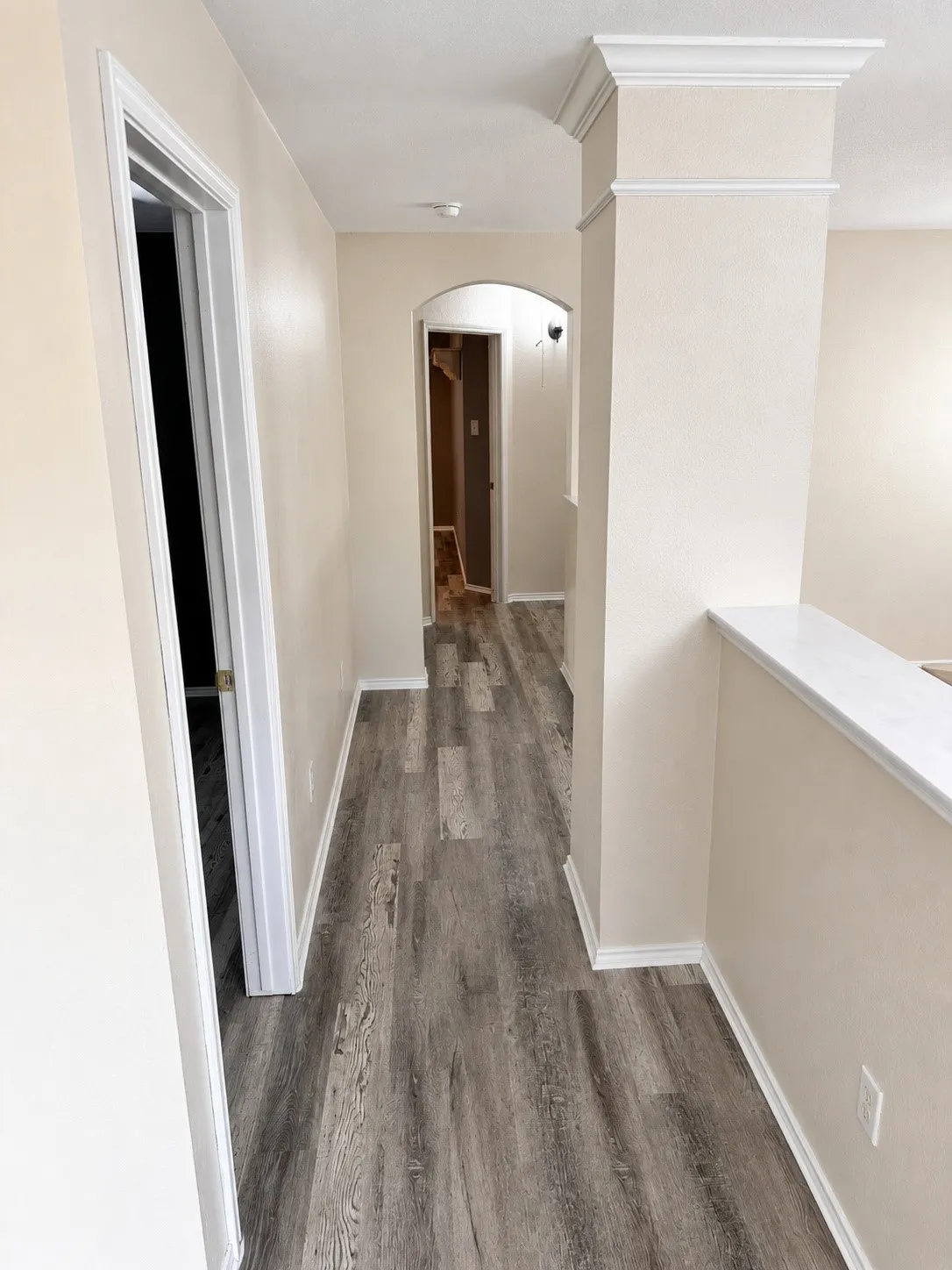 Hallway featuring wood-finish flooring, light neutral wall paint, white baseboards, and white door trim