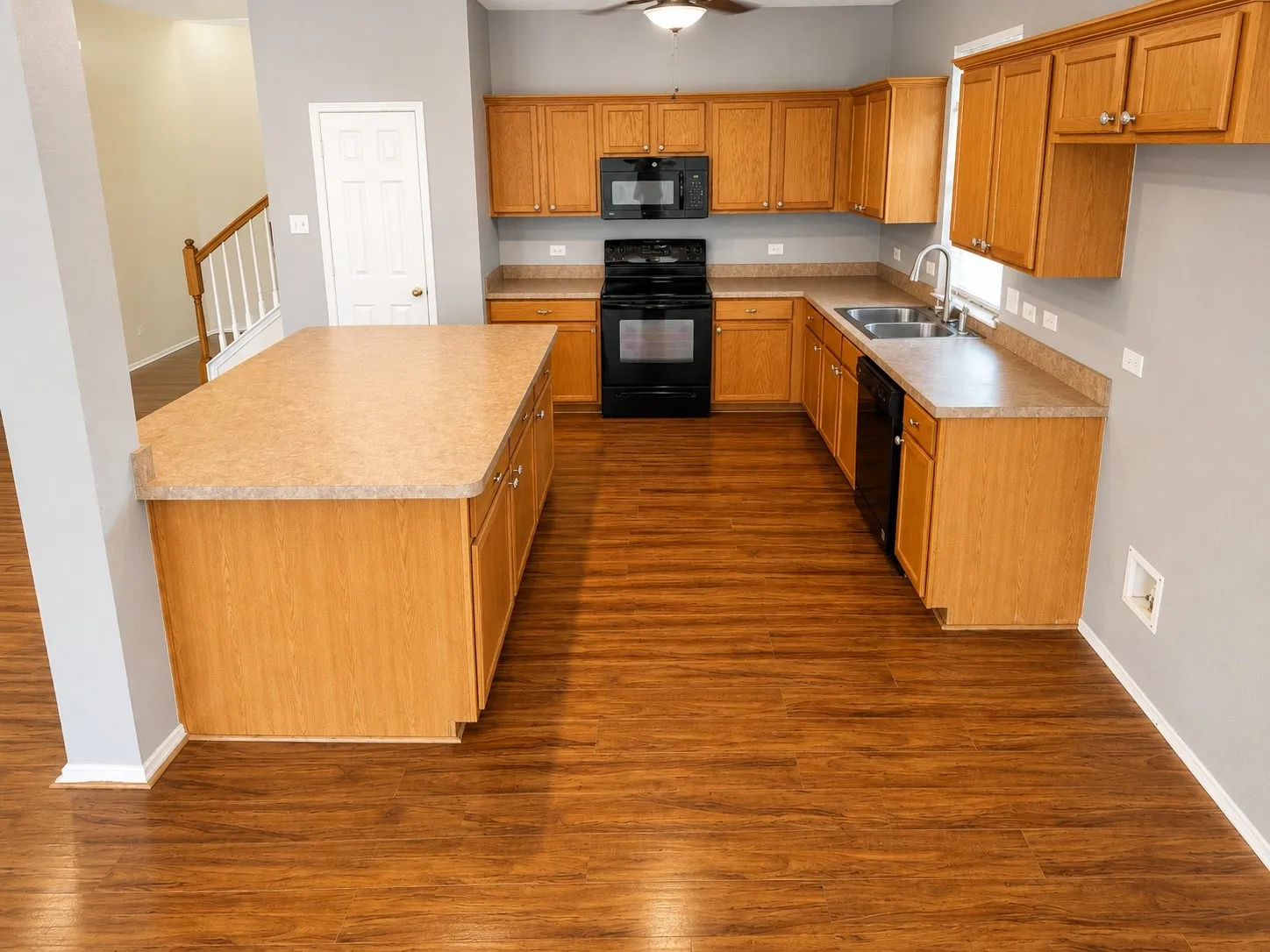 Kitchen featuring wood-finish flooring, a central island with countertop, coordinating wood cabinetry, black appliances including a range and microwave, and a double-basin sink with a gooseneck faucet