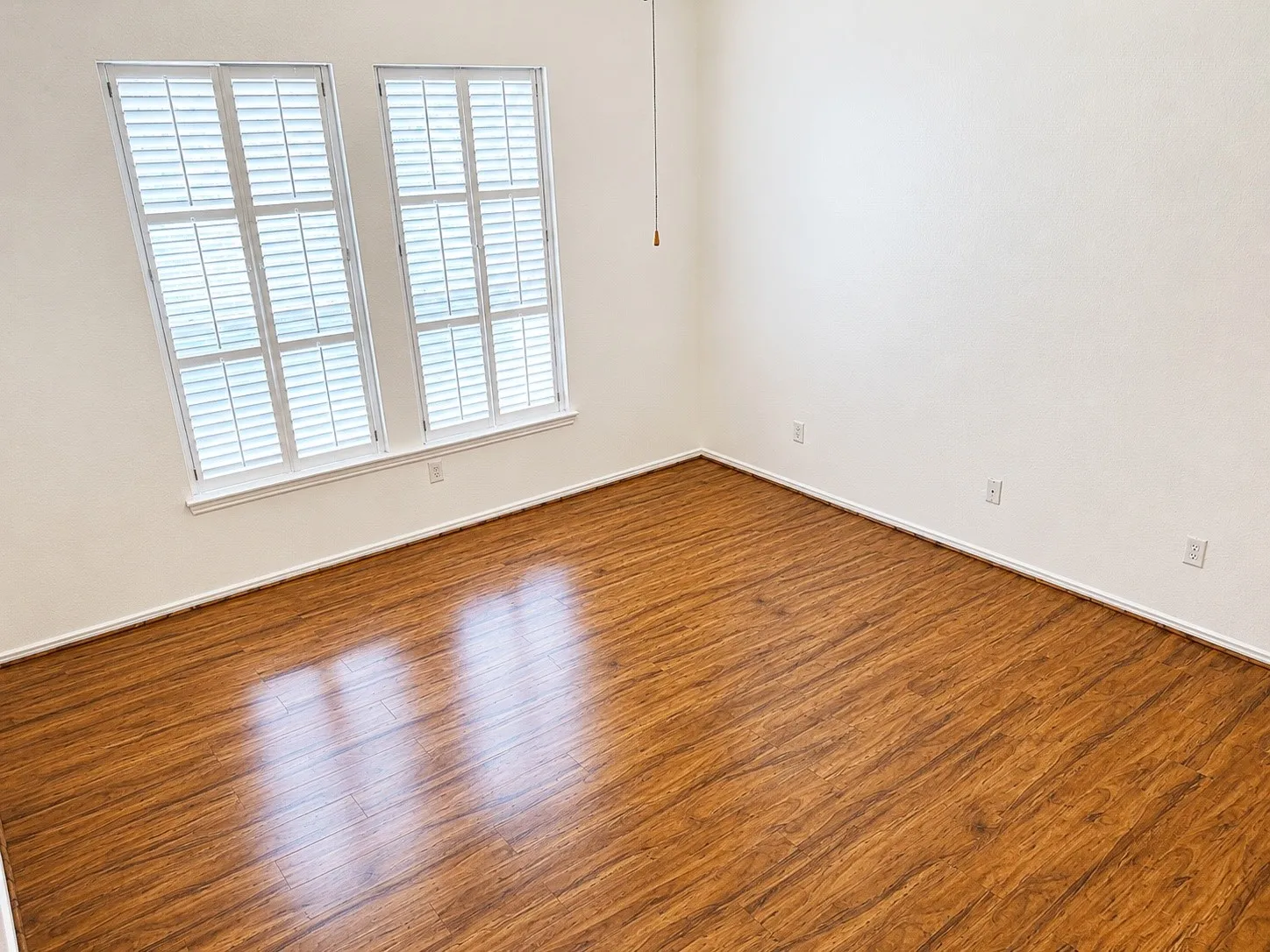 Spacious primary bedroom featuring wood-finish flooring, white baseboards, and bright white walls