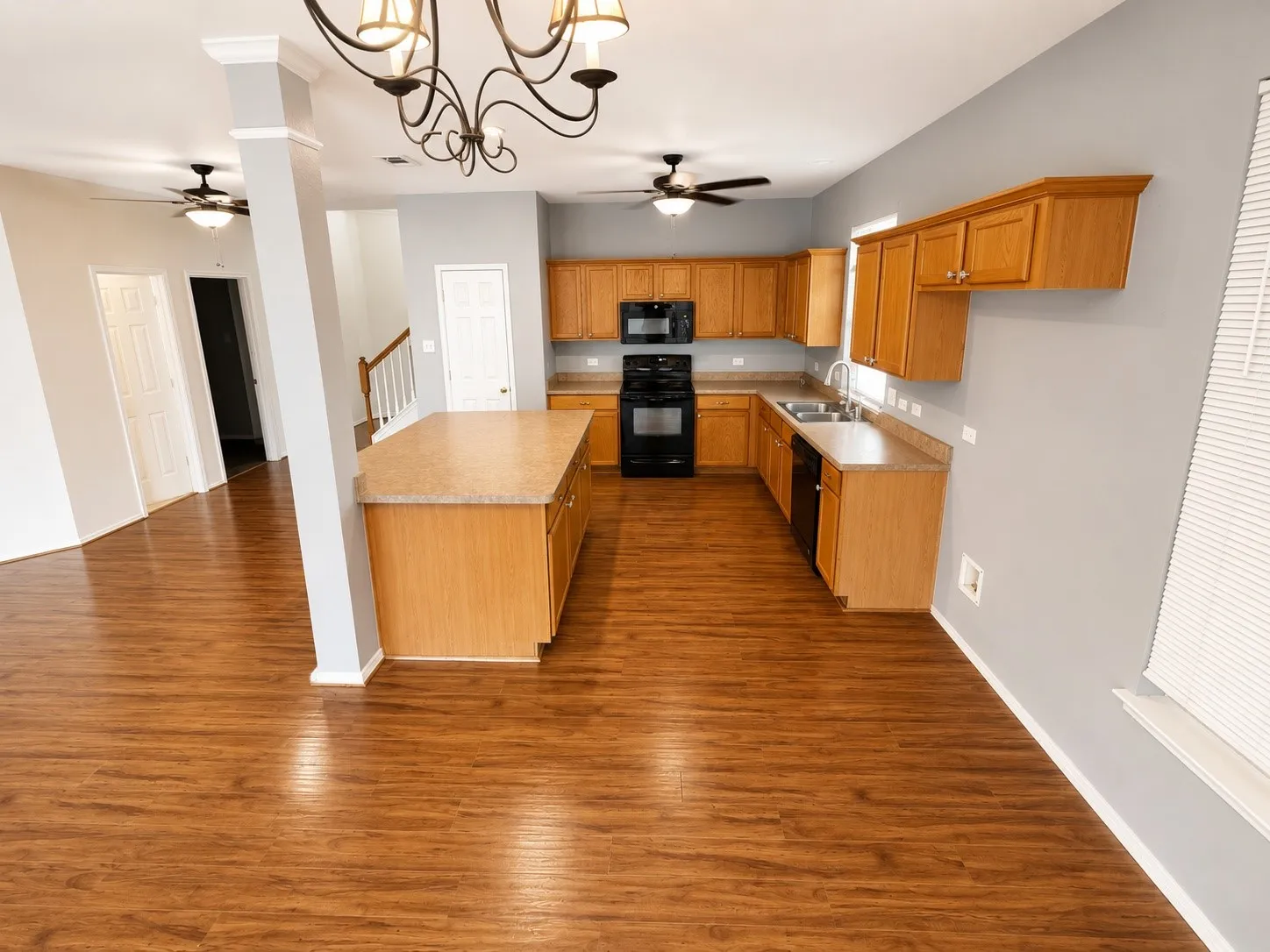 Open-concept kitchen featuring wood-finish flooring, a central island with countertop, natural wood cabinetry, and black appliances