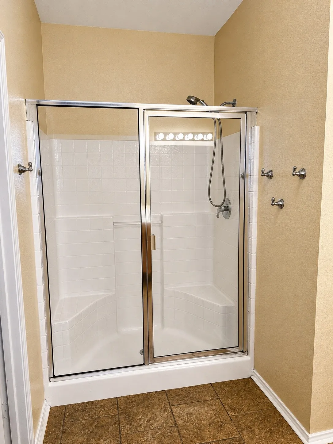 Enclosed shower featuring a handheld showerhead, built-in seating, and a glass sliding door