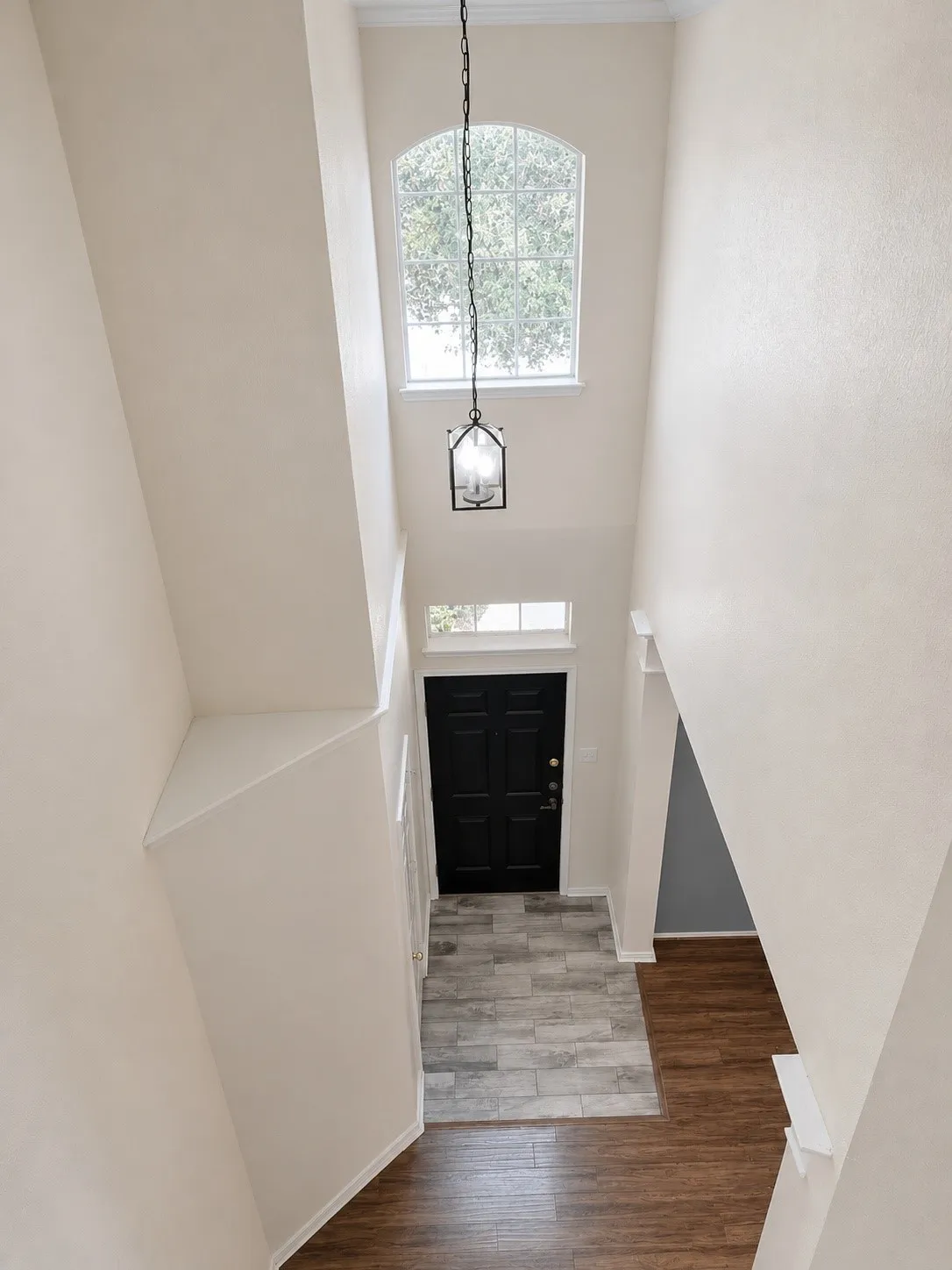 Two-story foyer featuring an arched window, a black lantern-style pendant light, a dark paneled entry door, and wood-finish flooring with a tile entryway