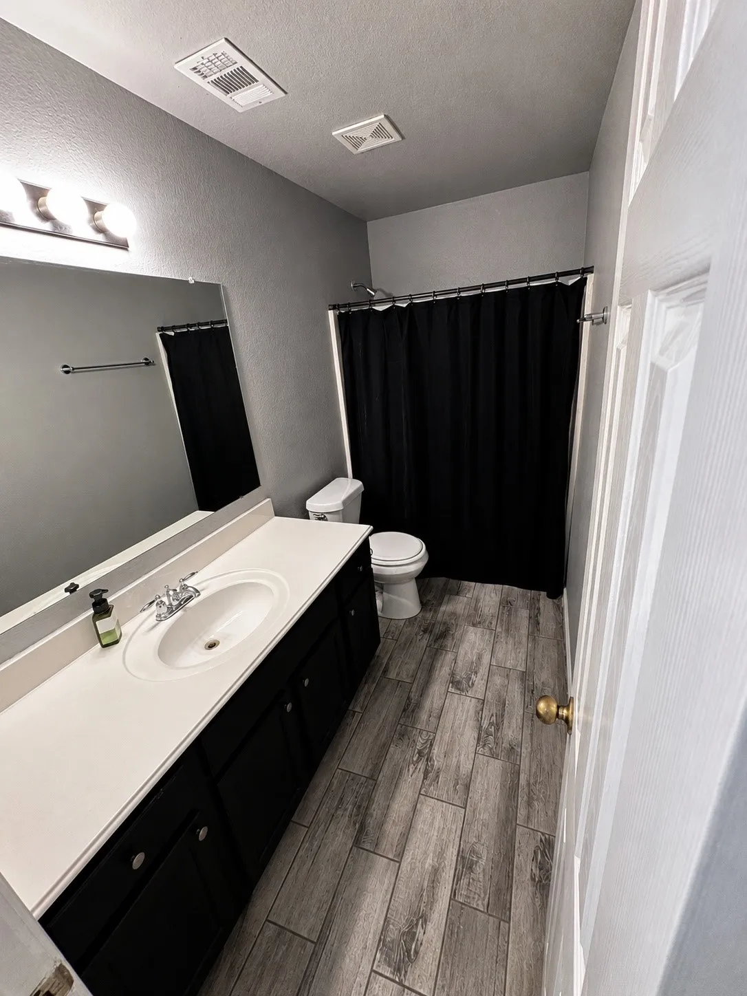 Bathroom featuring a white sink vanity with dark cabinetry, wood-finish flooring, and a shower with a black curtain