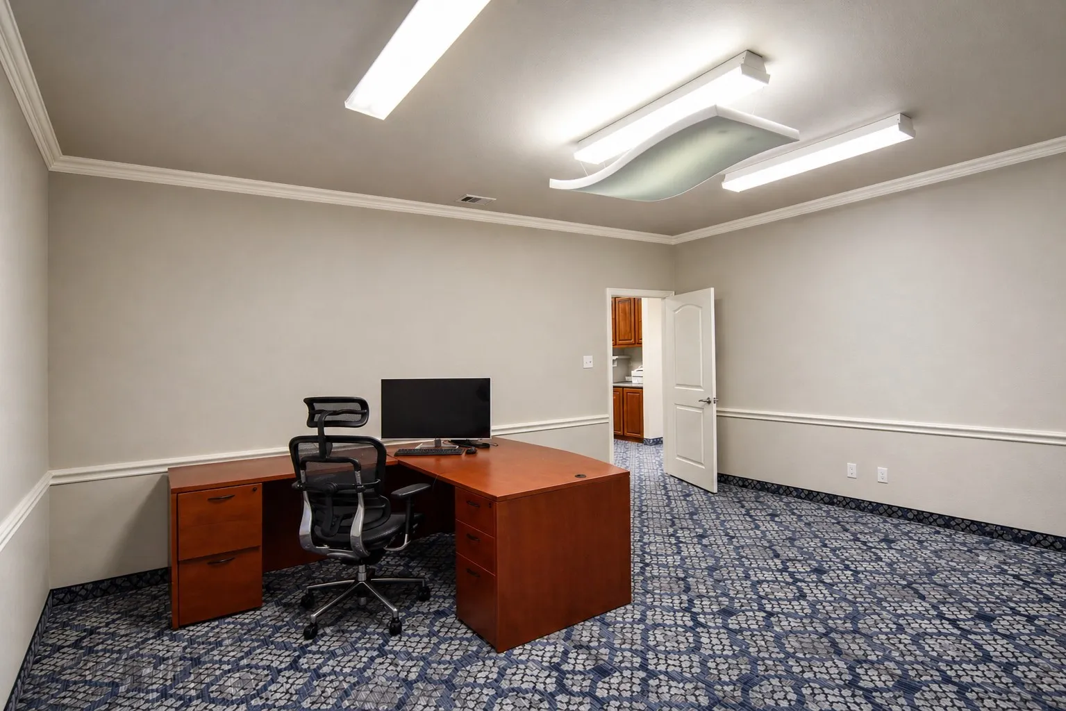 Spacious room featuring patterned blue carpeting, crown molding, chair rail molding, and a white paneled door