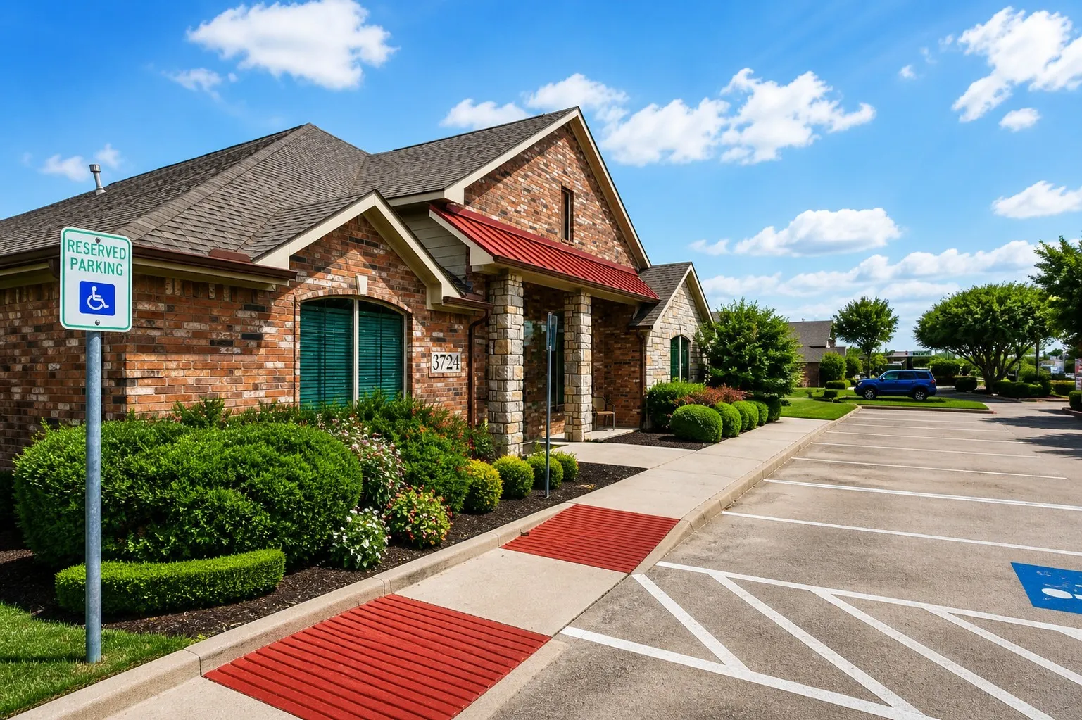Brick facade building featuring a gabled roof, covered entry, manicured landscaping, and designated parking area