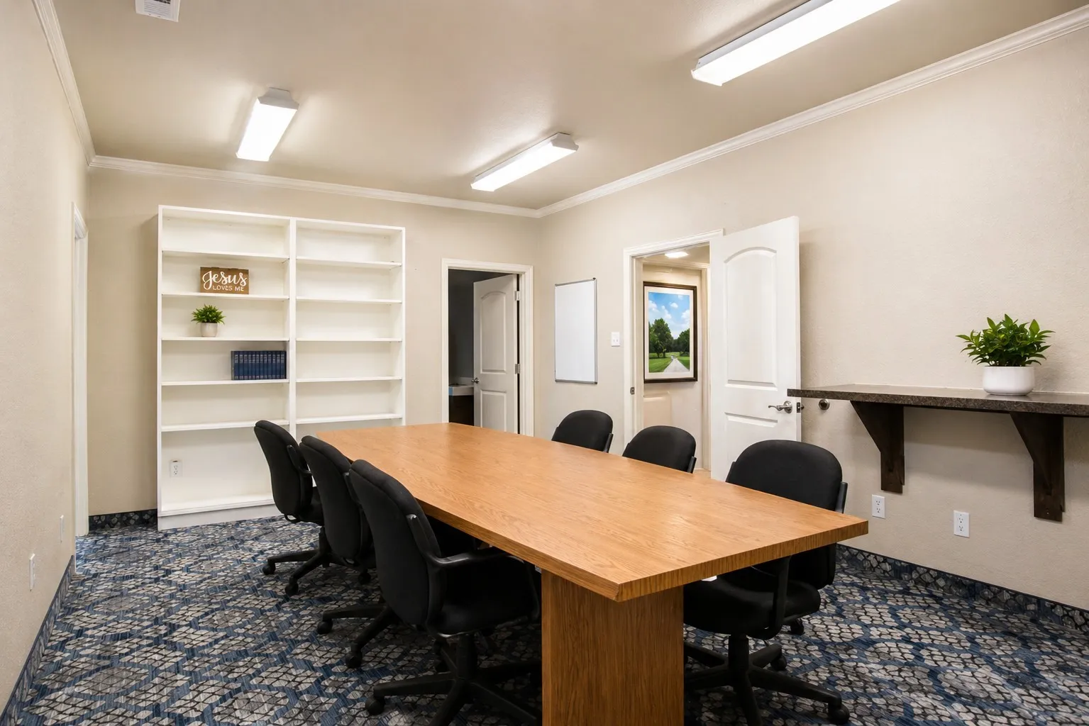 Spacious room with a large wooden table, built-in white shelving, crown molding, and patterned carpet flooring