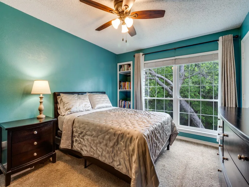 Primary bedroom with double closets, built-in bookshelf, and serene tree views.