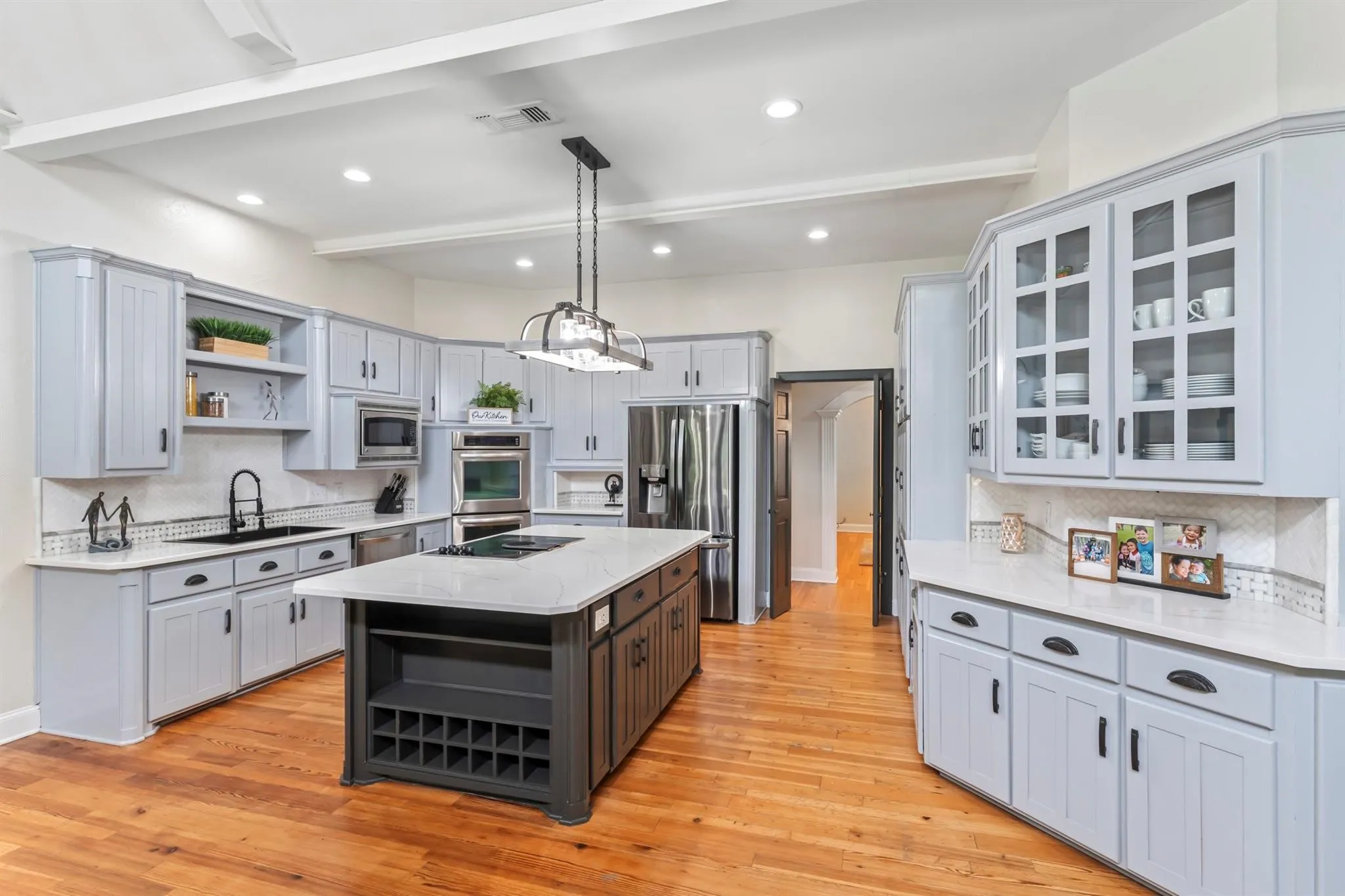 Dual tone kitchen with open shelves, tasteful backsplash, a center island, light stone countertops, and beamed ceiling