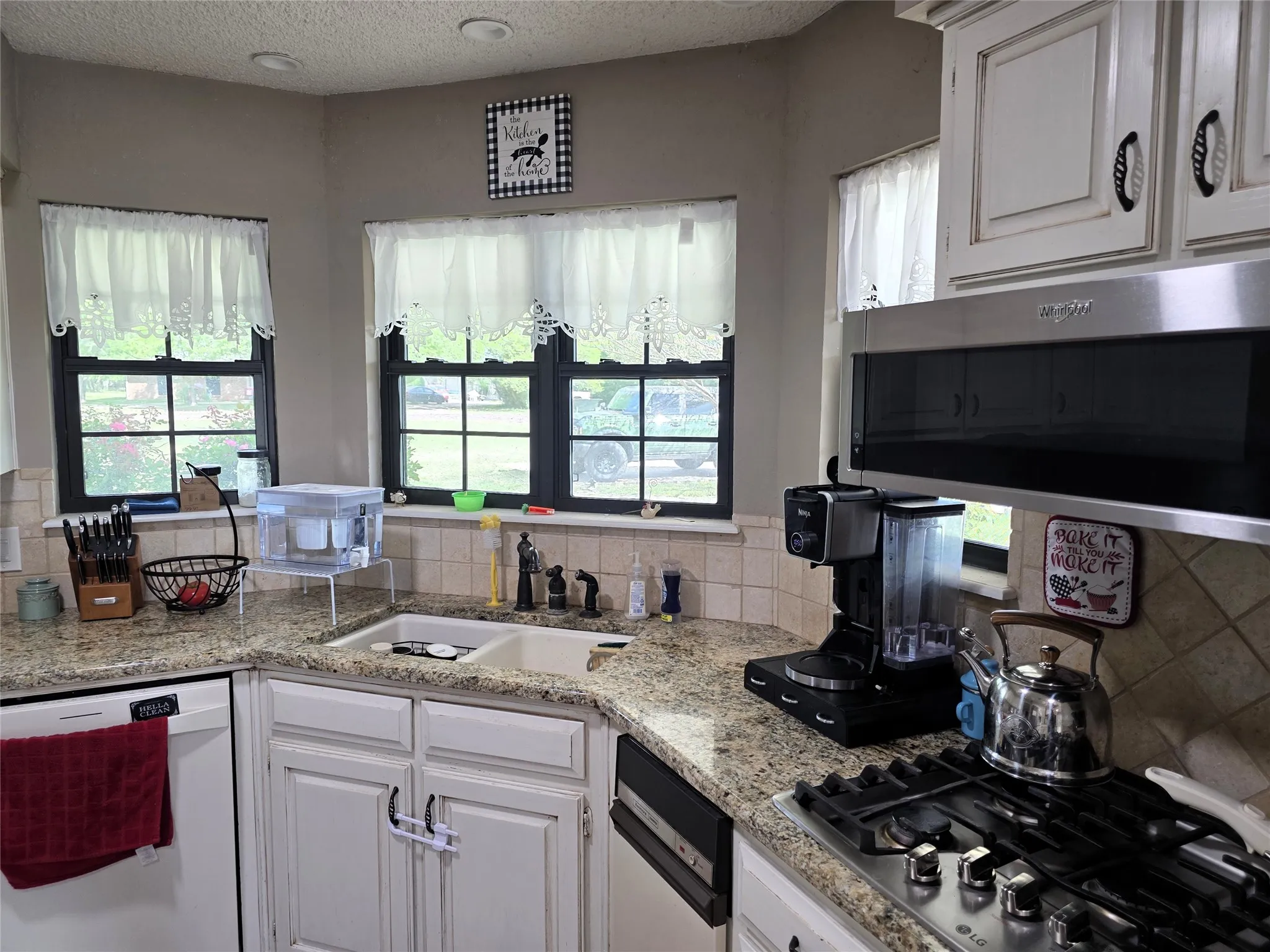 Kitchen featuring white cabinets, stainless steel appliances, a textured ceiling, light stone counters, and tasteful backsplash