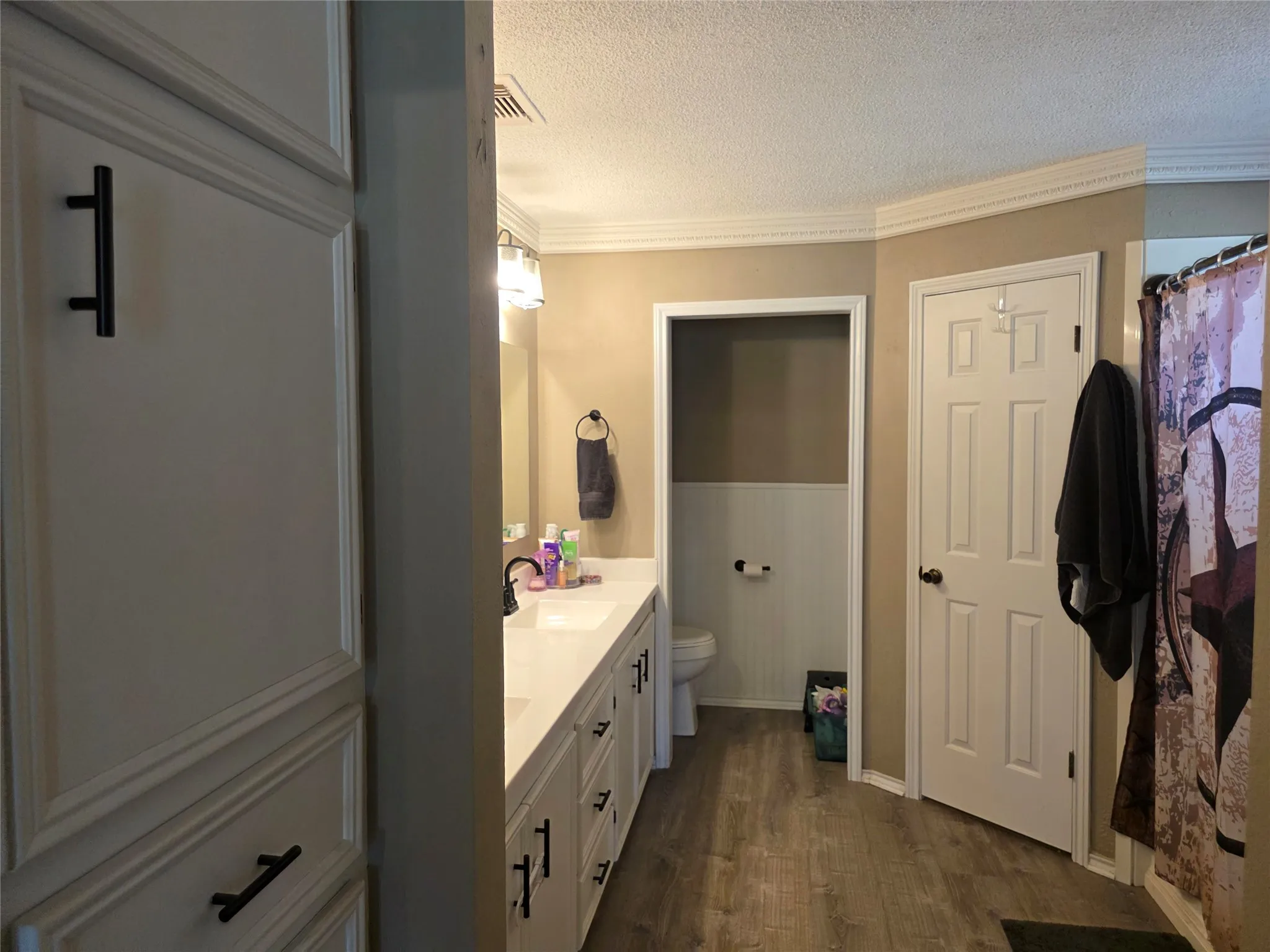 Full bath with double vanity, ornamental molding, a textured ceiling, dark wood-type flooring, and curtained shower
