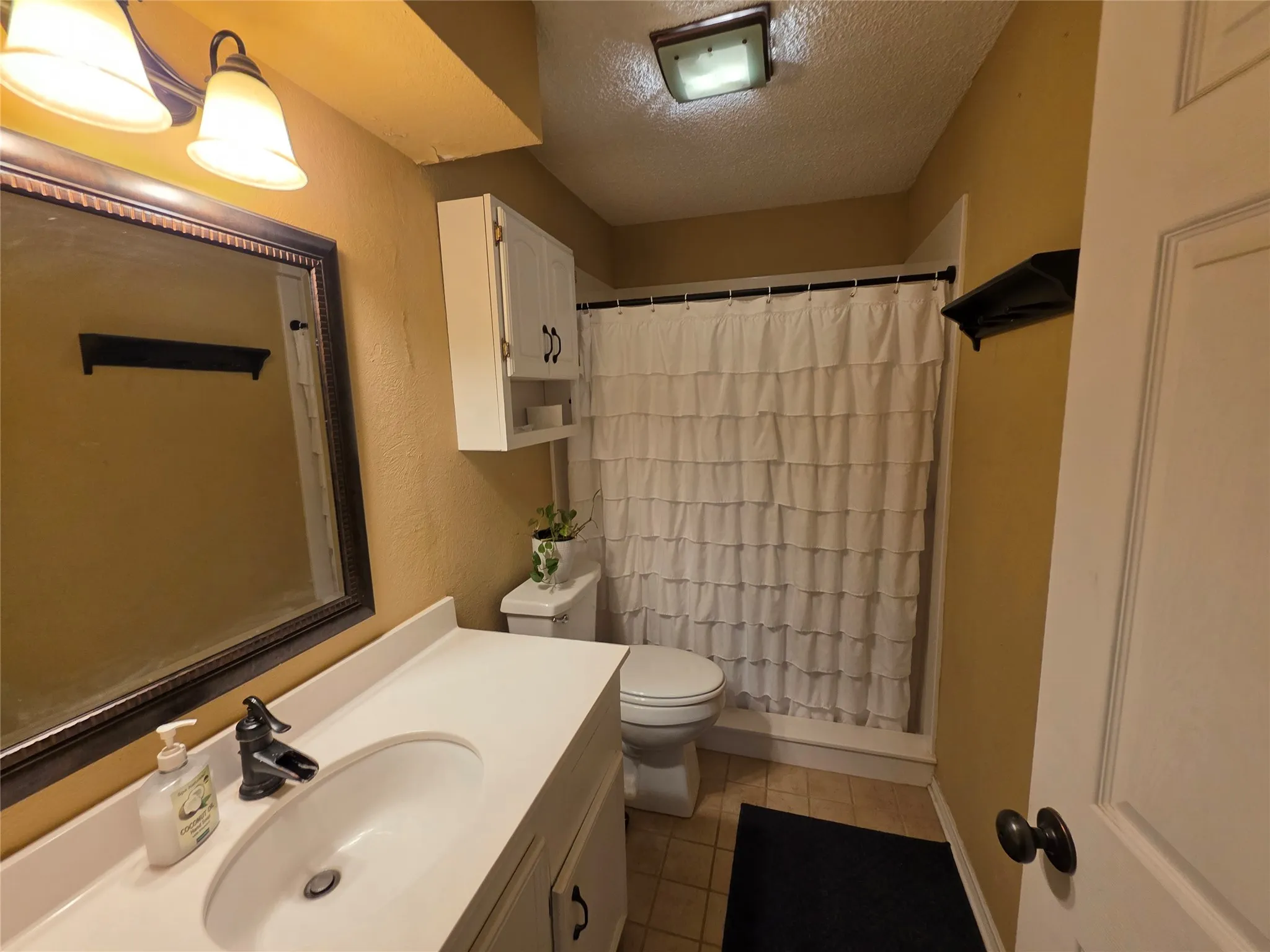 Full bathroom featuring a textured ceiling, vanity, and light tile patterned flooring
