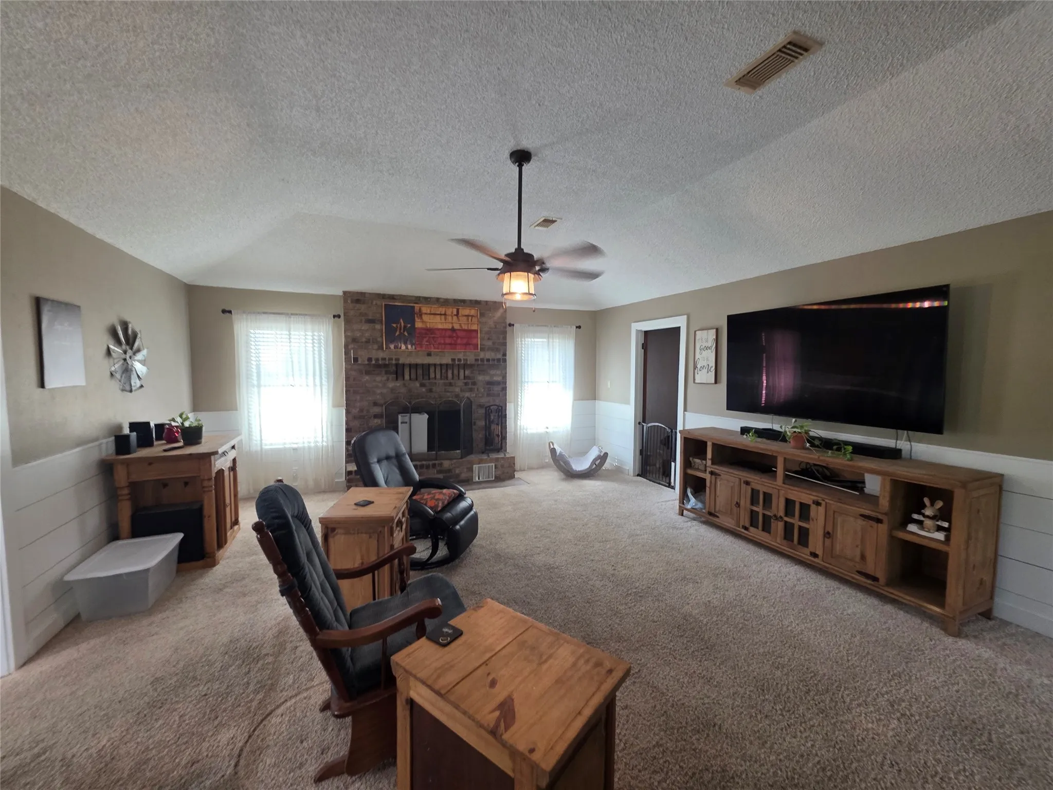 Carpeted living area featuring wainscoting, ceiling fan, a textured ceiling, and a fireplace