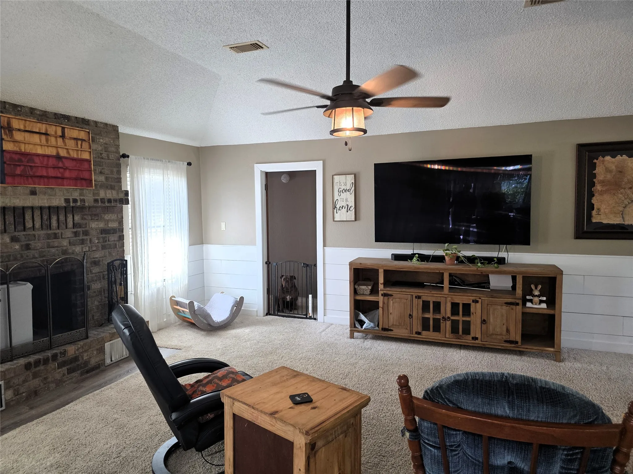 Living area featuring a wainscoted wall, carpet flooring, a brick fireplace, and ceiling fan