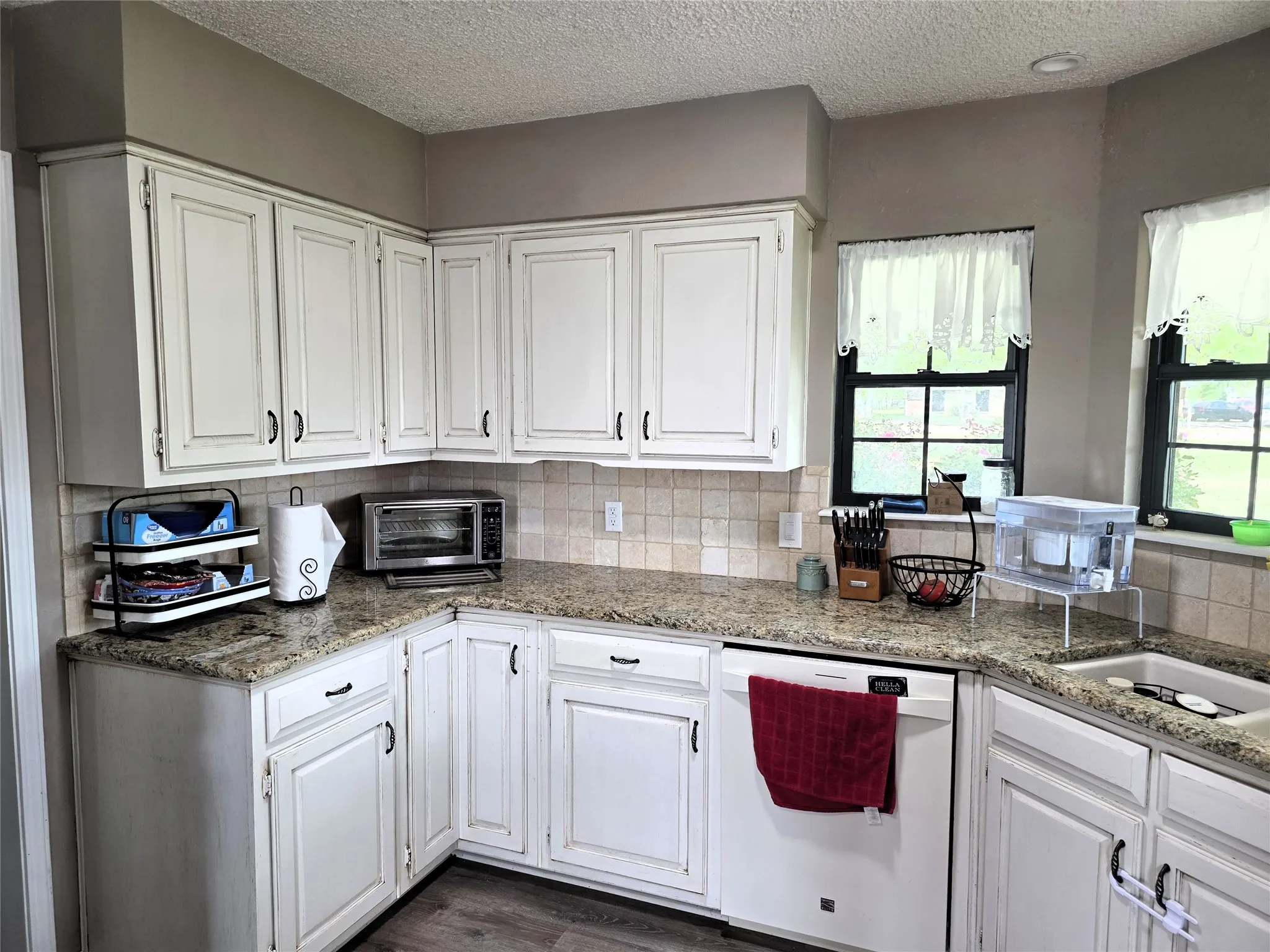 Kitchen with white cabinetry, dishwasher, a textured ceiling, light stone counters, and dark wood-style floors
