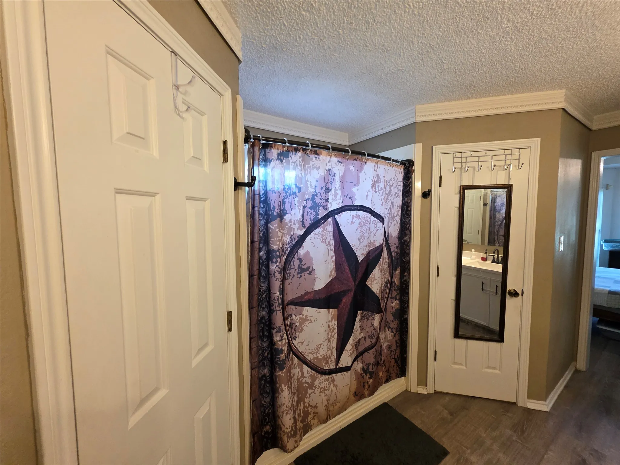 Ensuite bathroom with crown molding, a textured ceiling, dark wood-style floors, and curtained shower