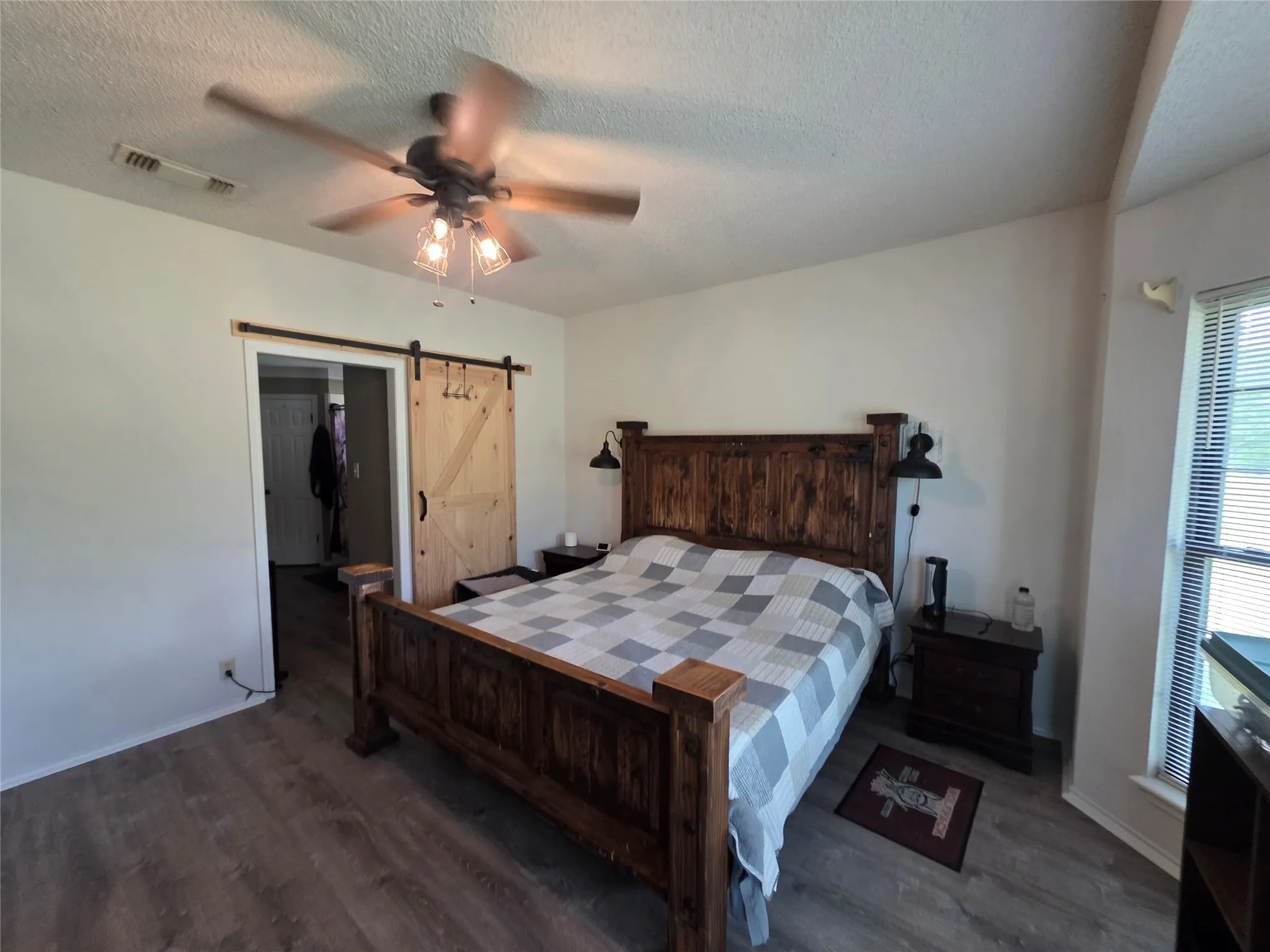 Bedroom with dark wood finished floors, a barn door, a textured ceiling, and a ceiling fan