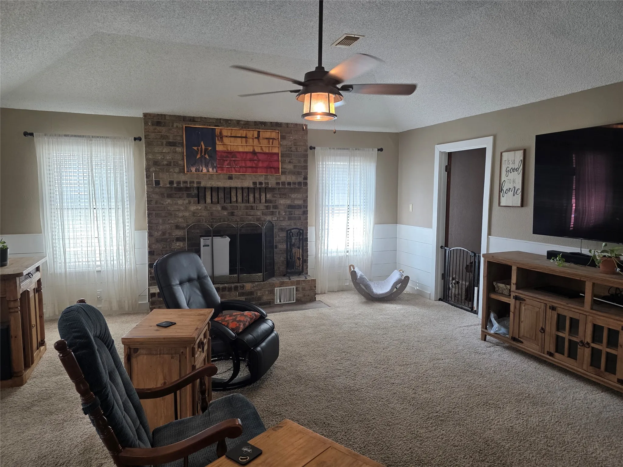 Carpeted living area featuring a textured ceiling, a ceiling fan, a wainscoted wall, and a fireplace
