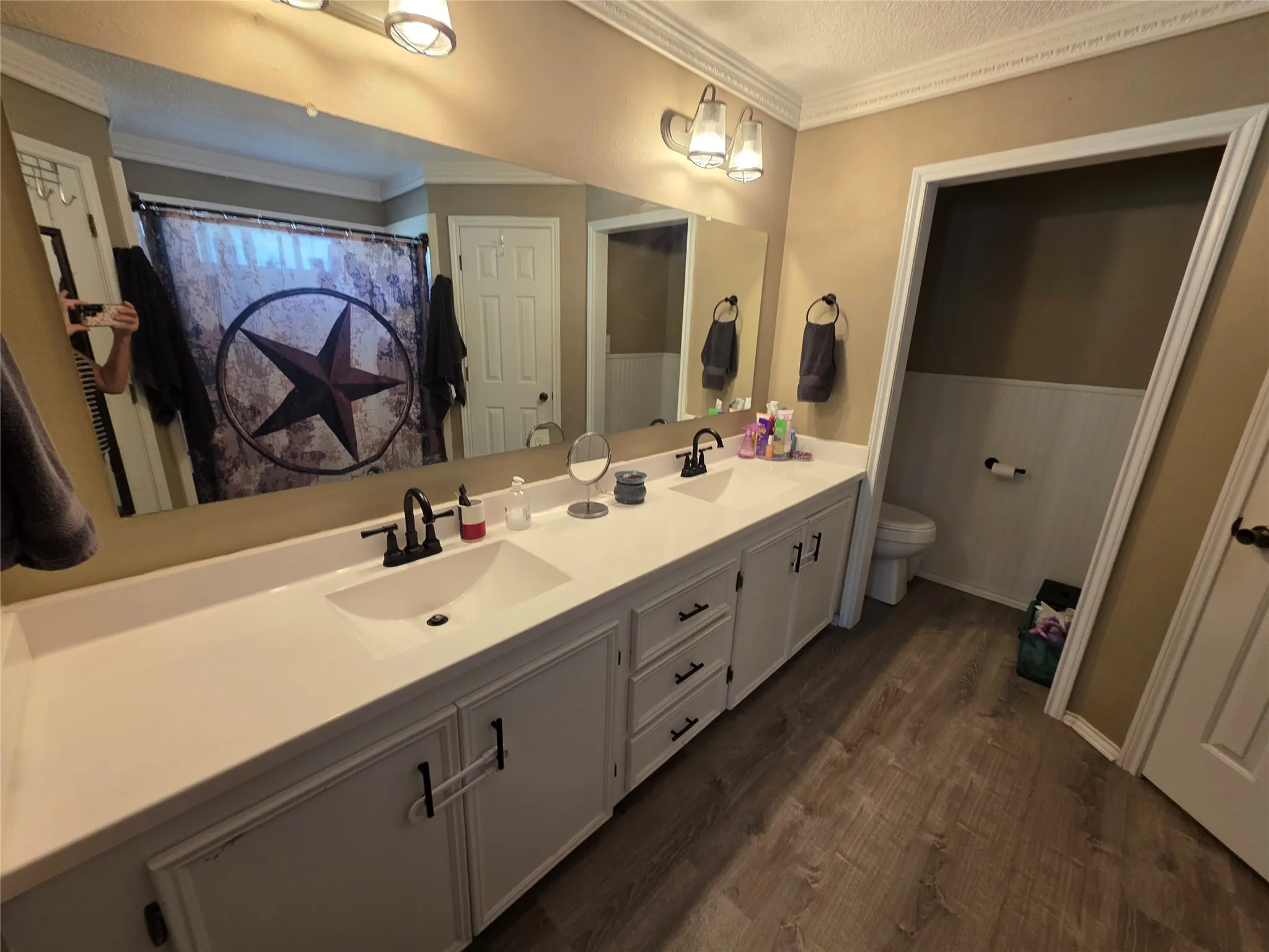 Full bathroom with double vanity, crown molding, dark wood-style floors, and curtained shower