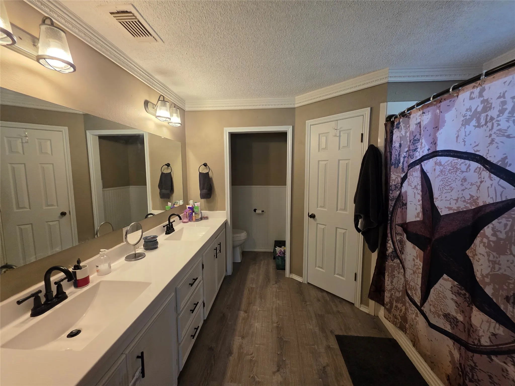 Full bath featuring double vanity, crown molding, a textured ceiling, a shower with shower curtain, and dark wood-style floors
