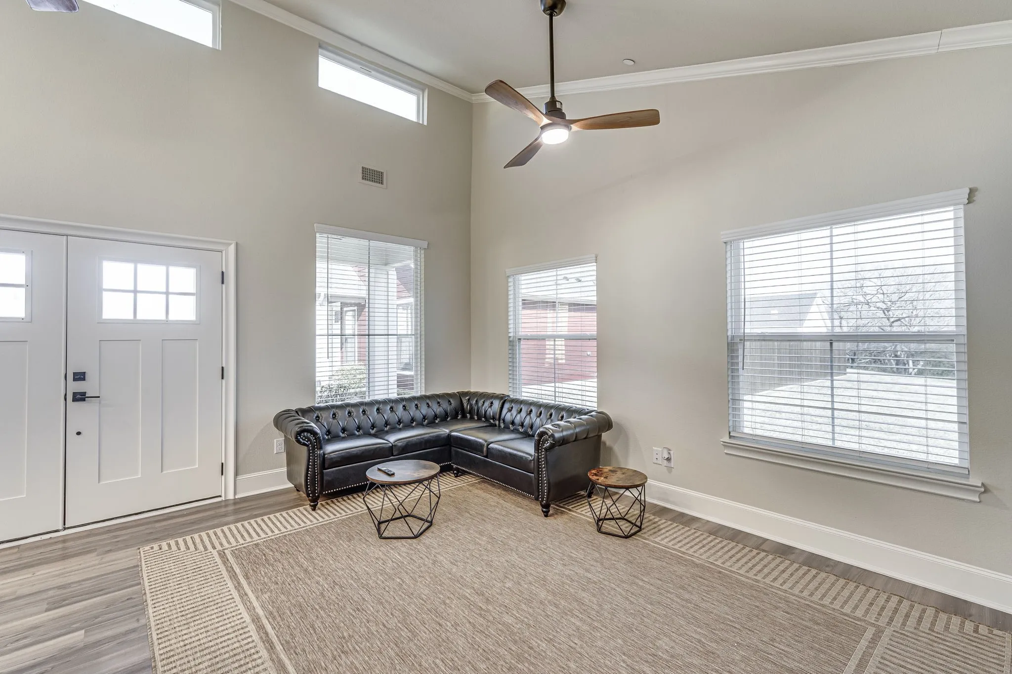 Living room featuring a high ceiling, a ceiling fan, crown molding, and wood finished floors