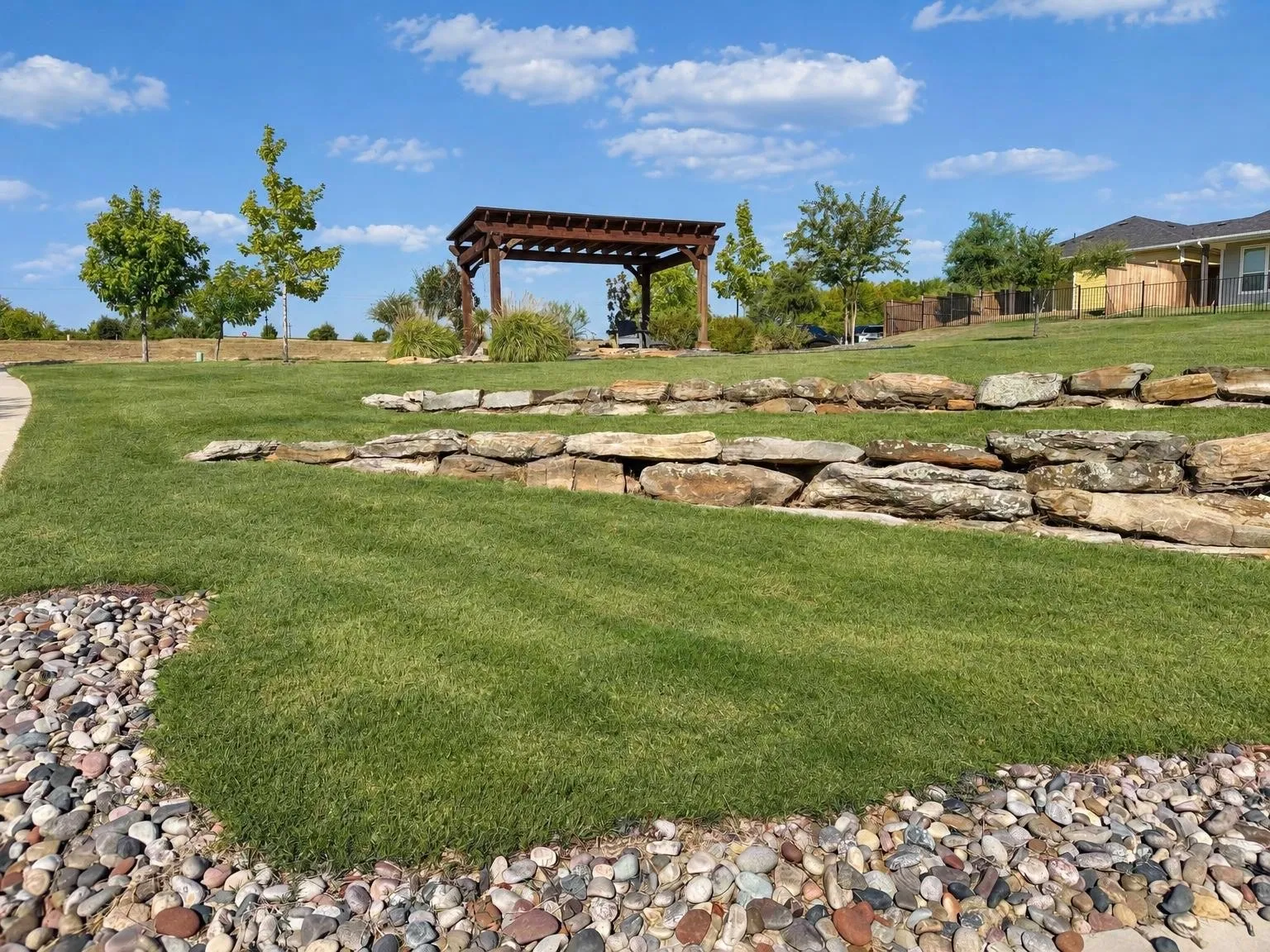 Landscaped grounds featuring a wooden pergola, retaining walls crafted from natural stone, and a winding paved pathway
