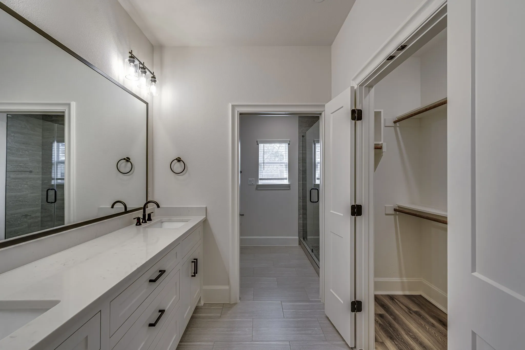 Full bathroom with double vanity, a walk in closet, a shower stall, and light wood-style flooring