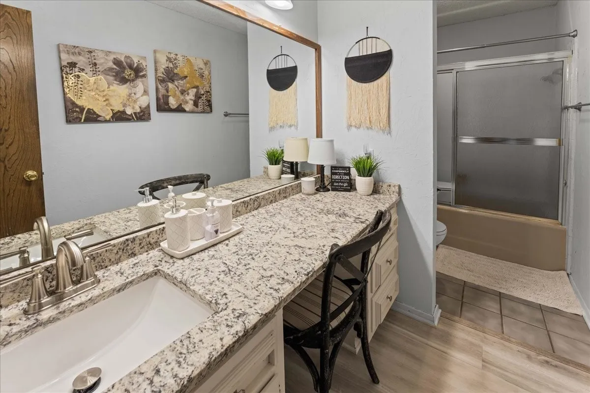 Bathroom with bath / shower combo with glass door, vanity, and light wood-style flooring