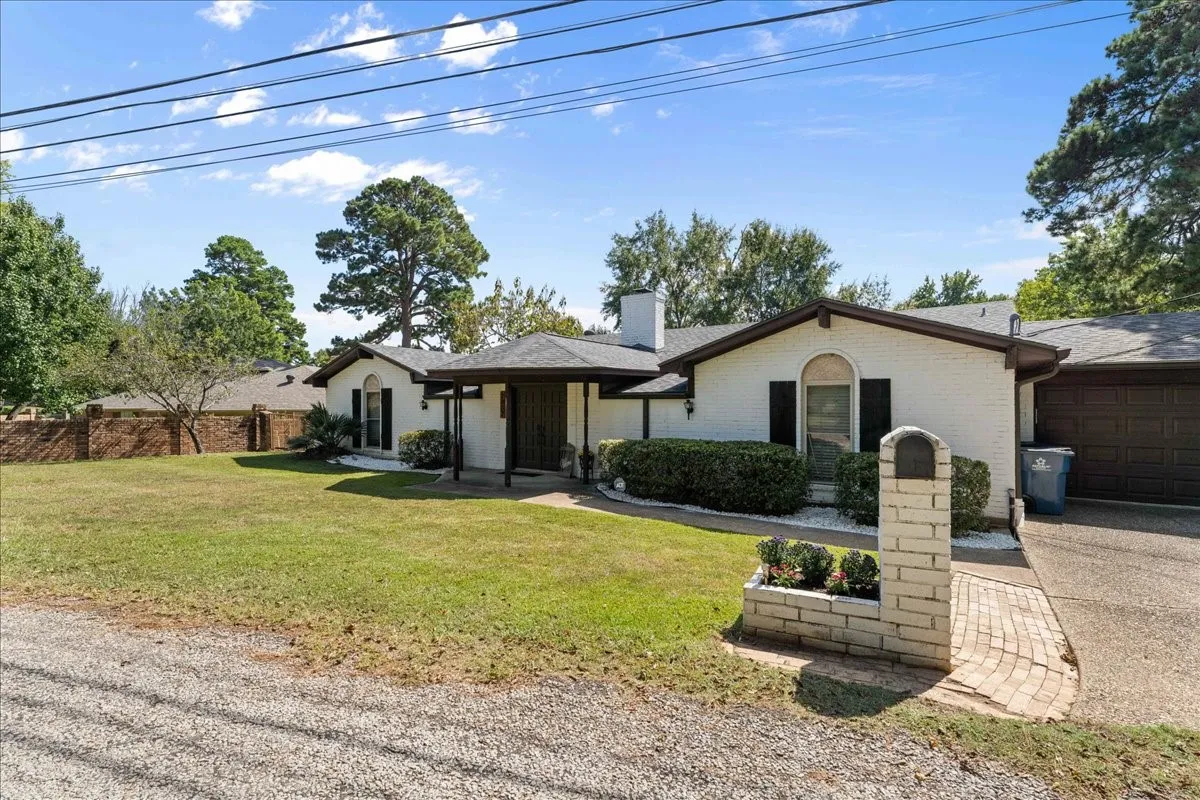 Ranch-style house featuring a chimney, an attached garage, driveway, and brick siding