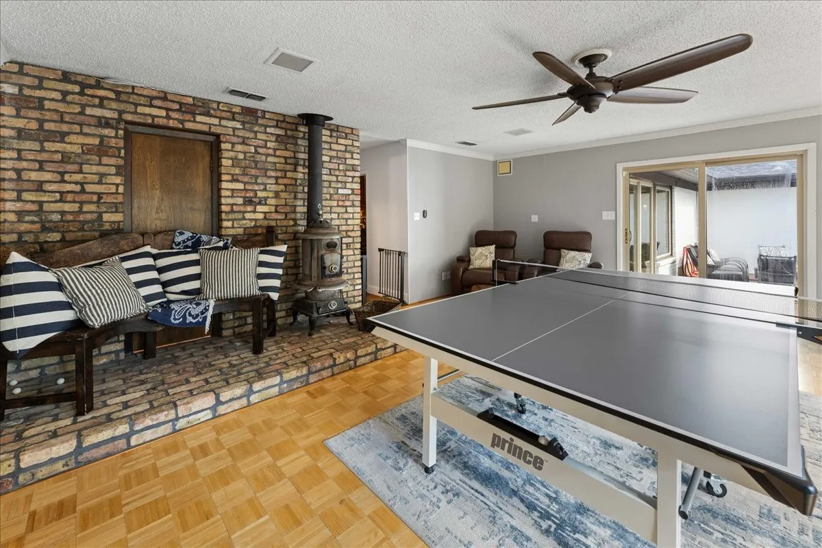 Recreation room with a wood stove, a textured ceiling, ornamental molding, a ceiling fan, and brick wall