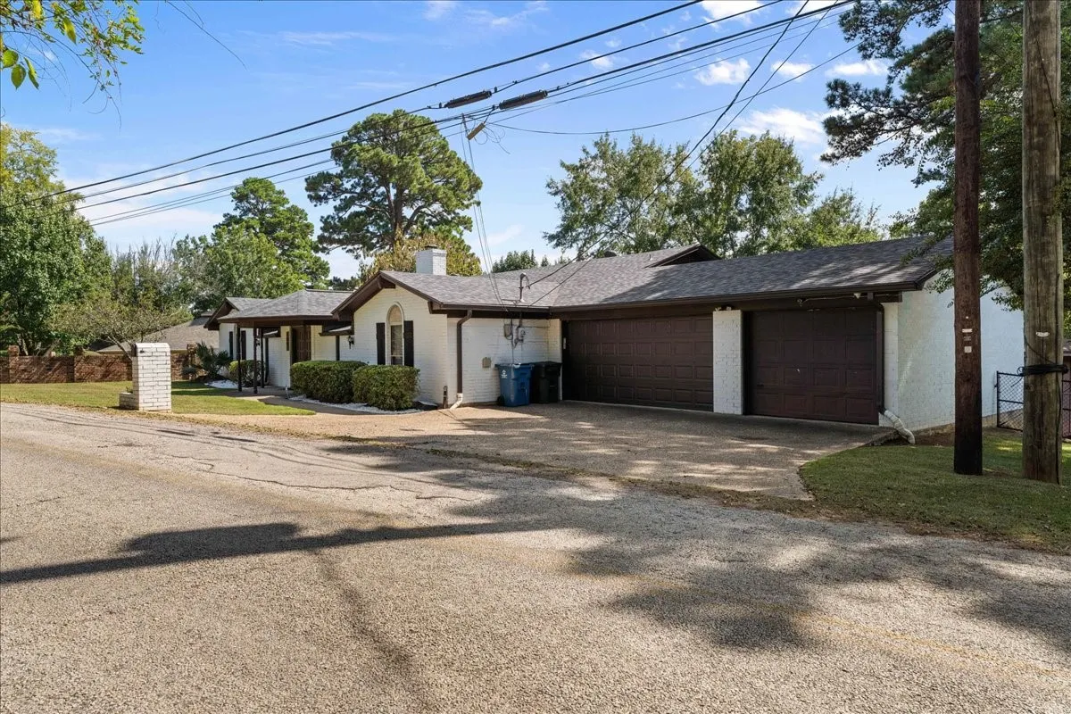 Ranch-style home featuring an attached garage, a chimney, driveway, and brick siding