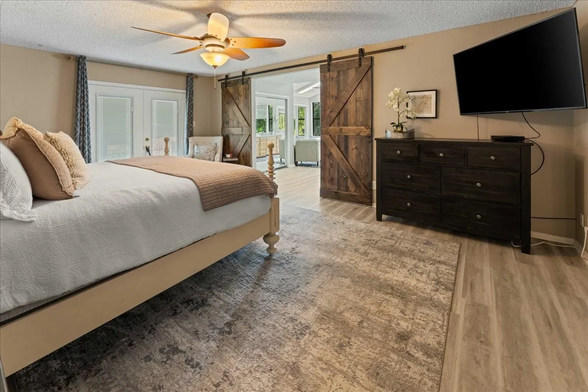 Bedroom with a textured ceiling, a barn door, light wood-style floors, and a ceiling fan