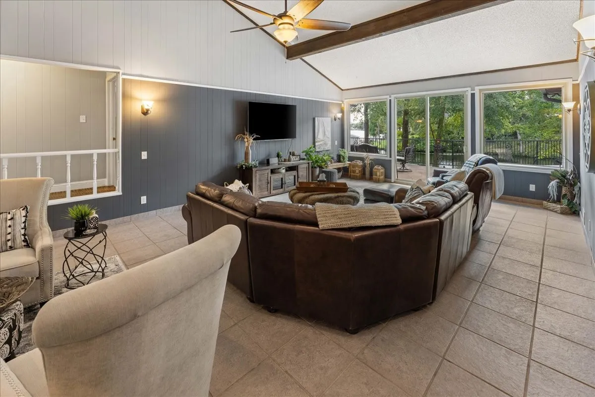 Living area featuring light tile patterned floors, ceiling fan, and wooden walls