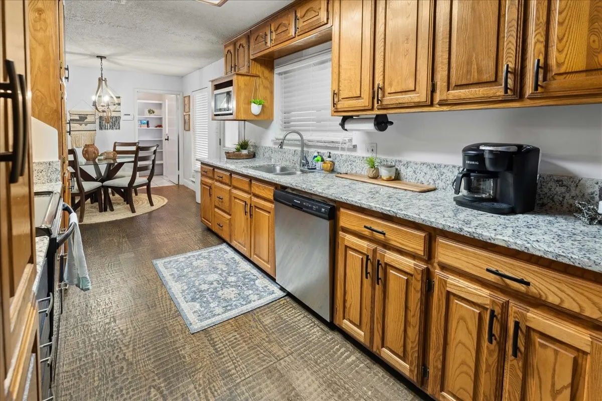 Kitchen with brown cabinetry, light stone countertops, decorative light fixtures, appliances with stainless steel finishes, and a textured ceiling