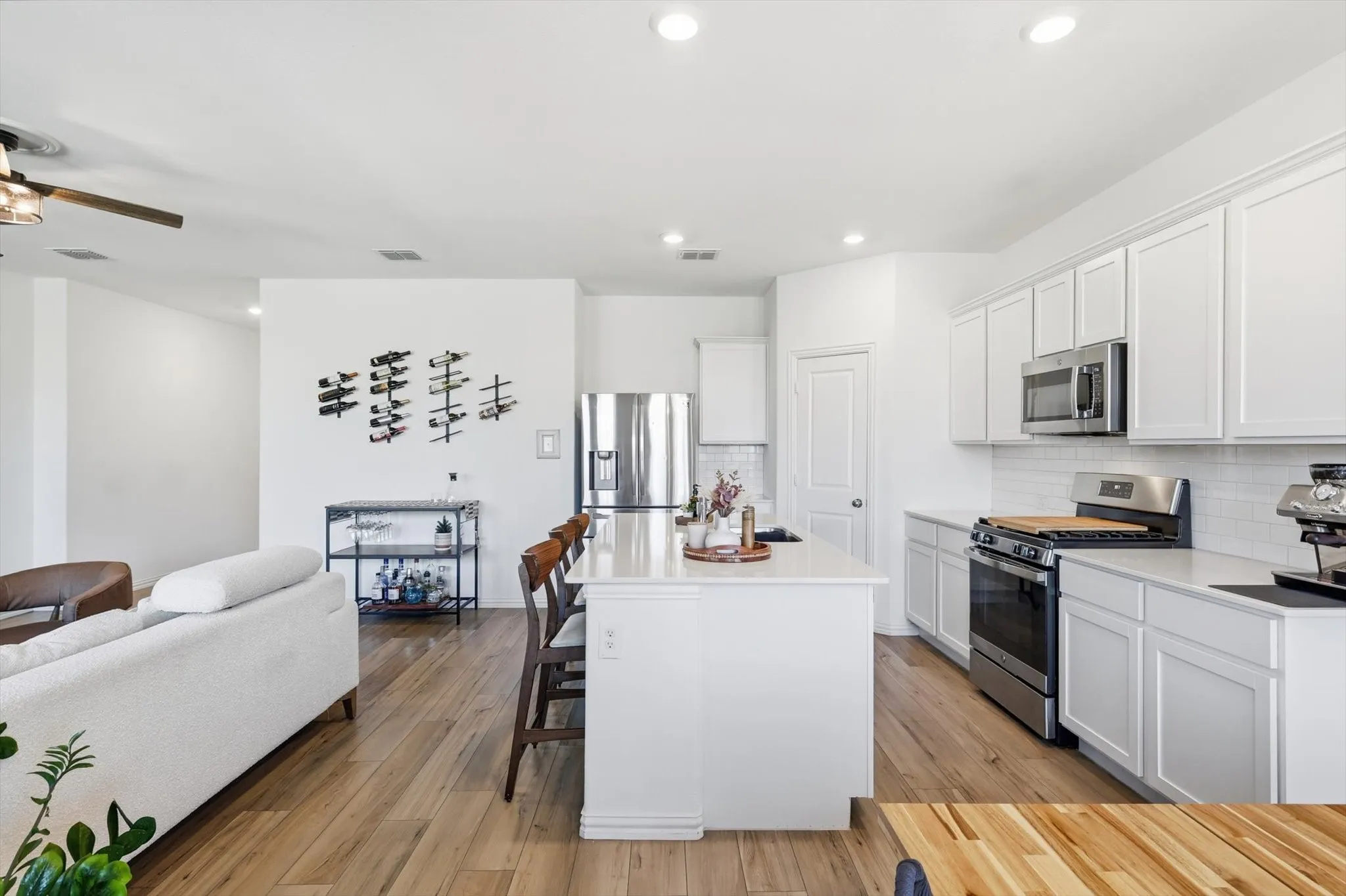 Kitchen with stainless steel appliances, a kitchen breakfast bar, white cabinets, light LVP flooring, and decorative backsplash